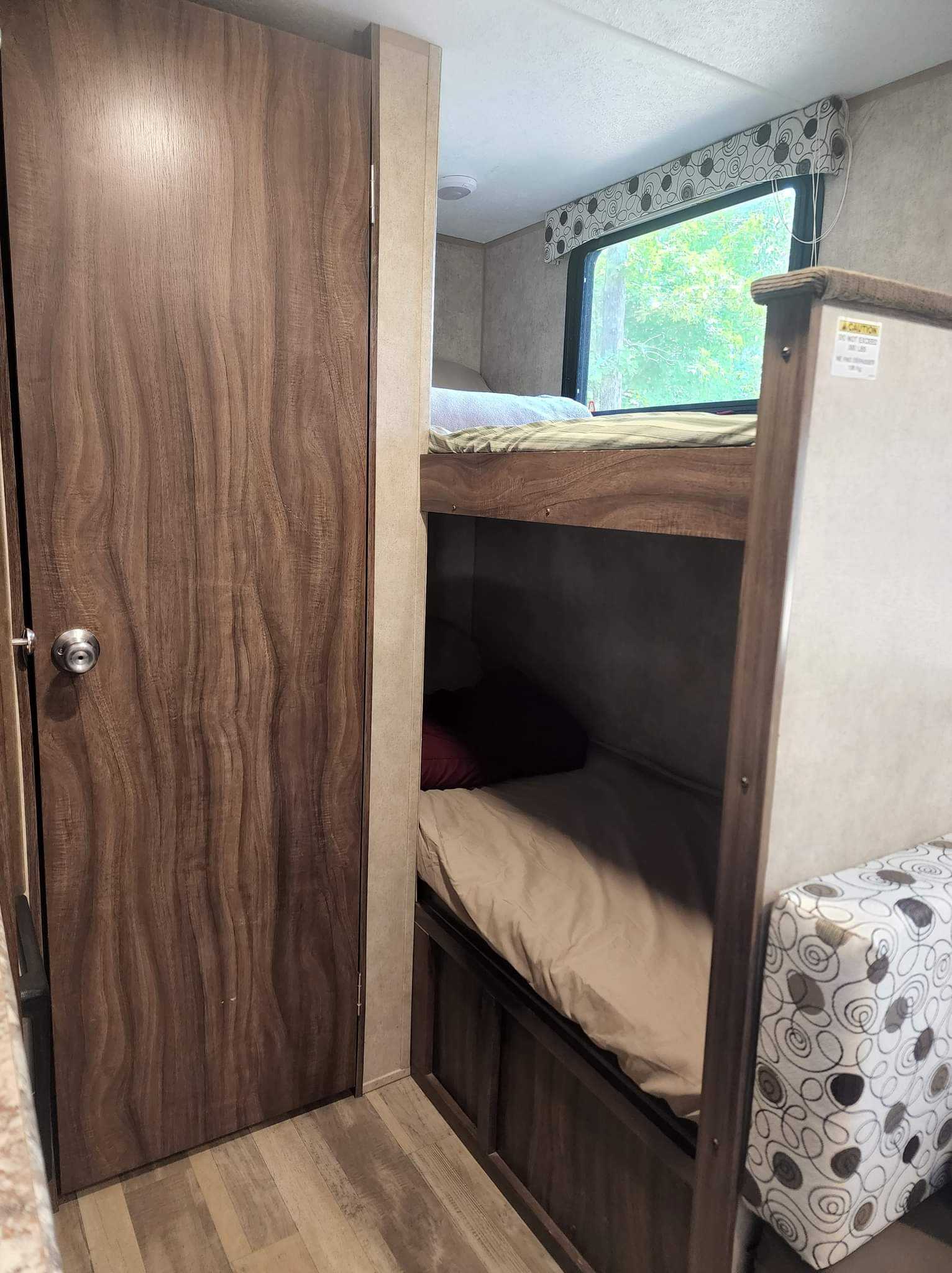 RV rental interior shows a wood-grain door on left, bunk beds with bedding on right, and window view.. Clipper Cadet 2017