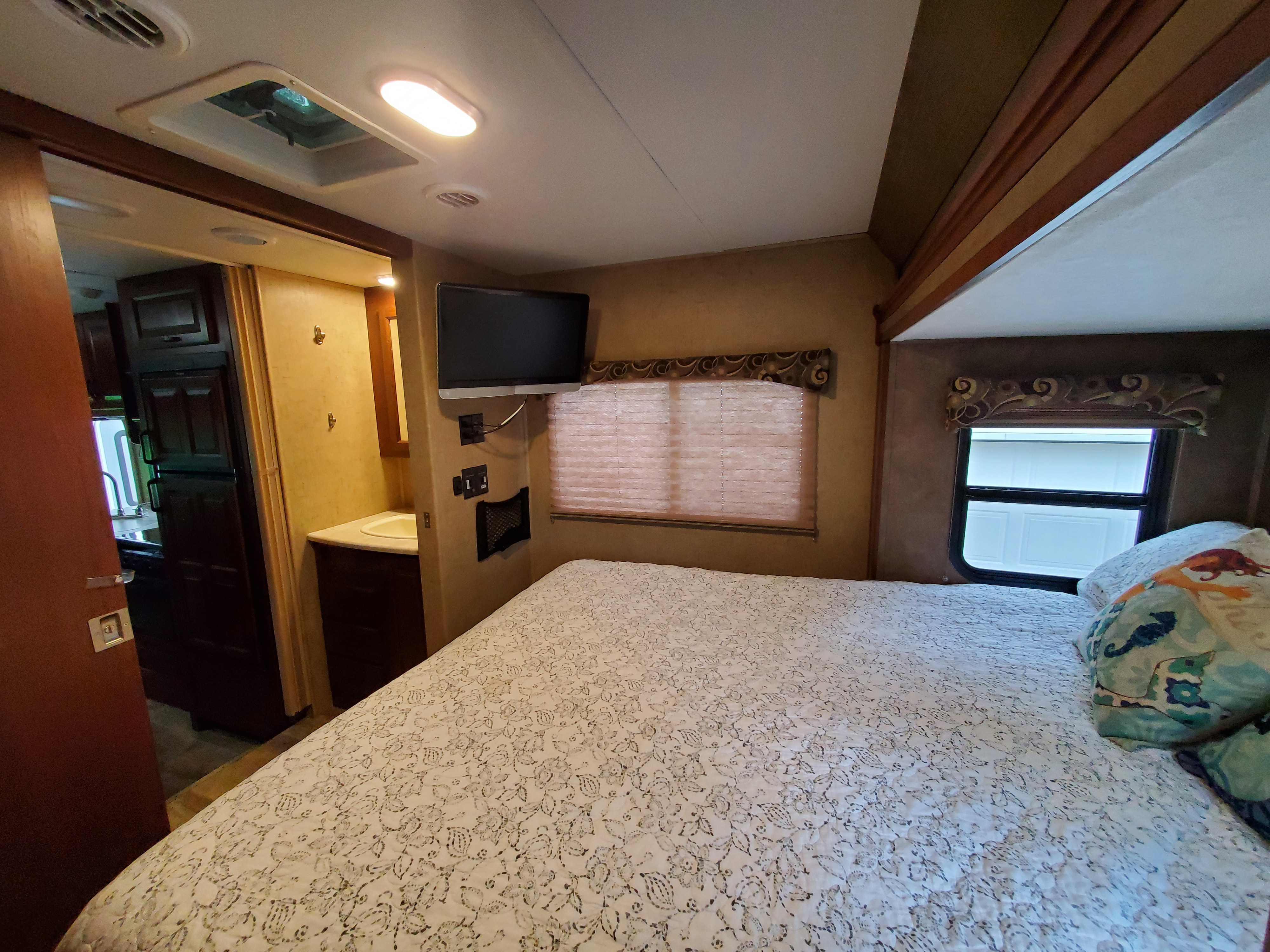 Cozy RV rental bedroom featuring a comfortable bed, wall-mounted TV, and a nearby bathroom/kitchen access.. Forest River Sunseeker 2016