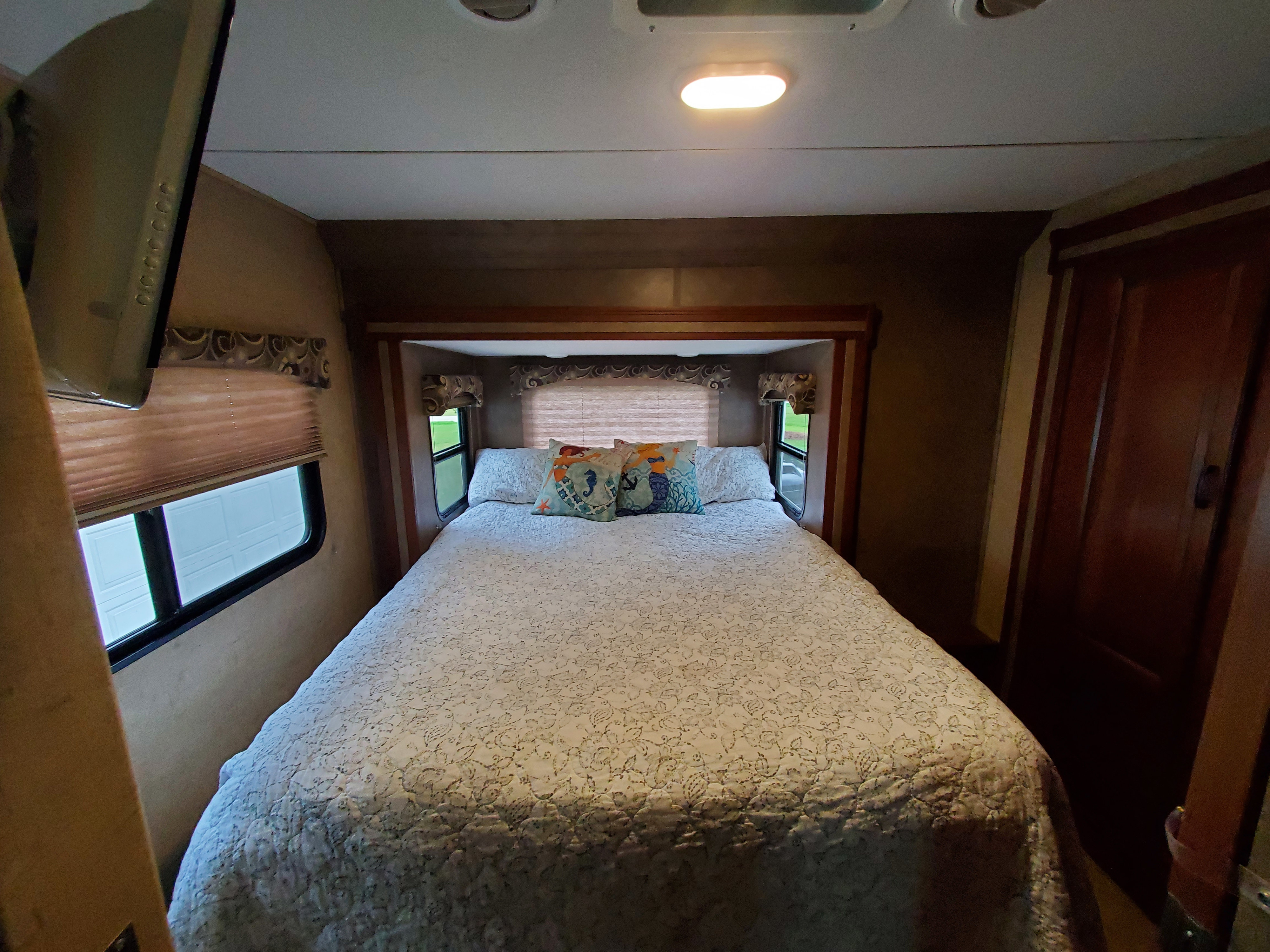 Step into comfort: a cozy RV rental bedroom featuring a full bed, windows, and mounted TV for your travel needs.. Forest River Sunseeker 2016