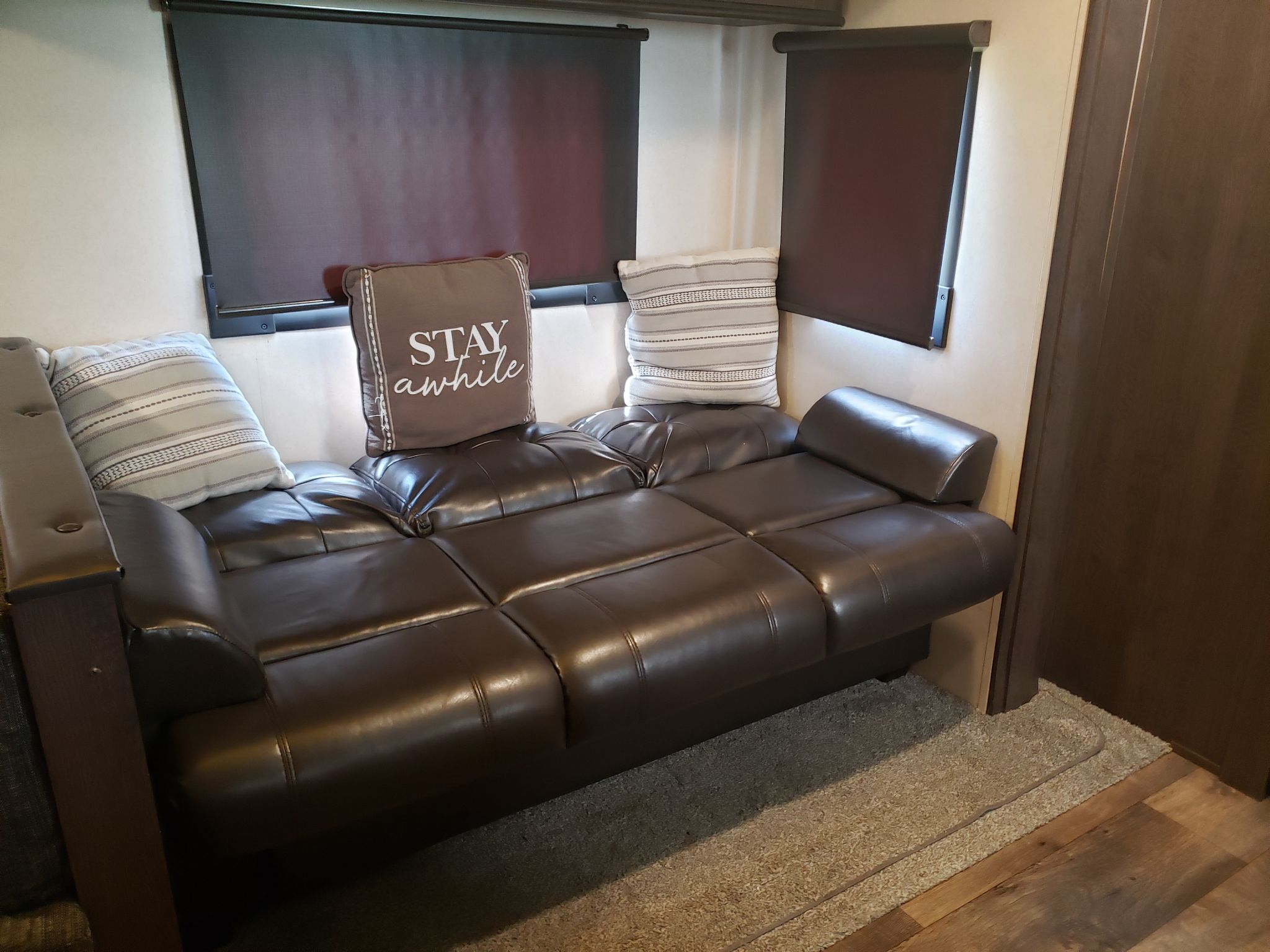 Cozy RV rental living area featuring a brown sofa with decorative pillows, set against walls with dark window shades.. Forest River Salem 2018