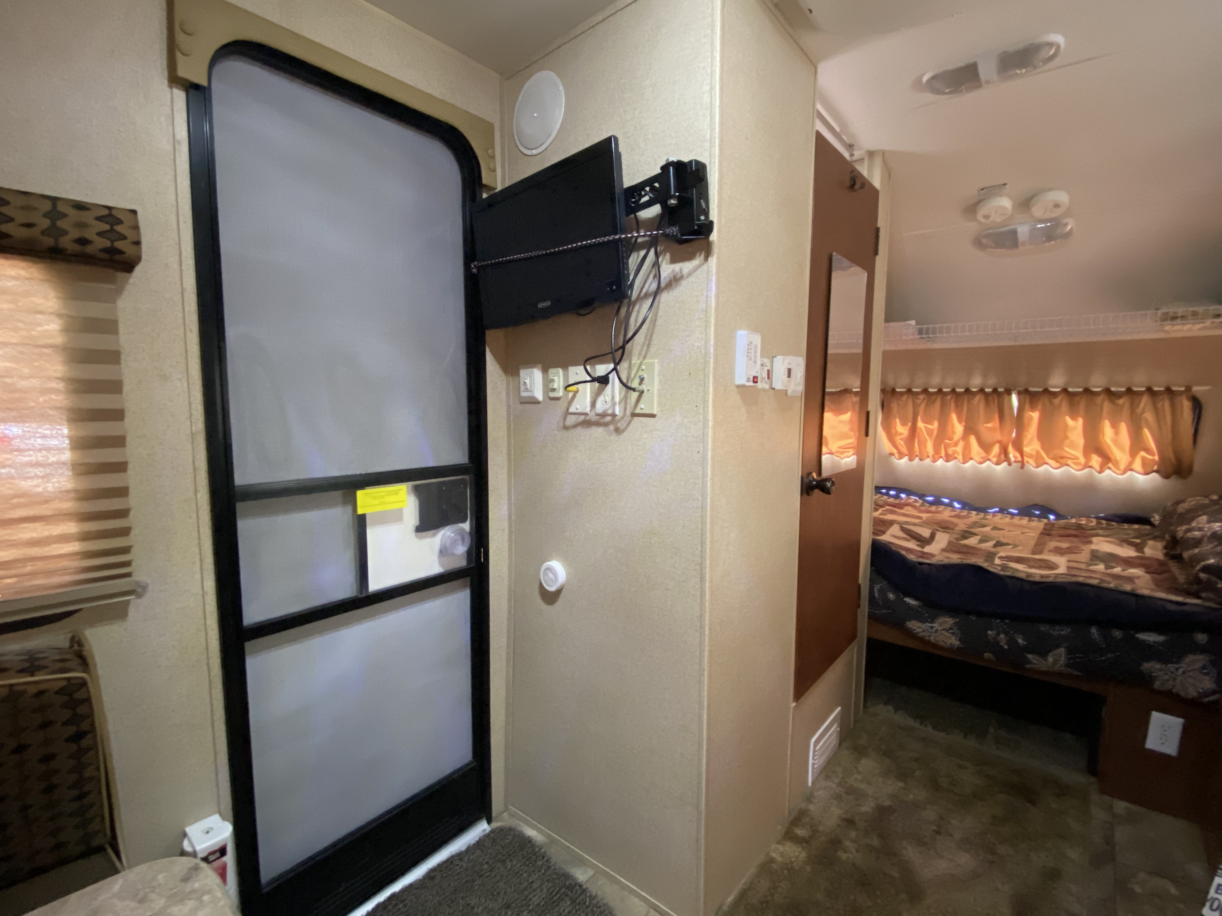 RV rental interior: cozy bedroom, entry door, wall-mounted TV, and various controls, offering a comfortable space.. Forest River RPod 177 2014