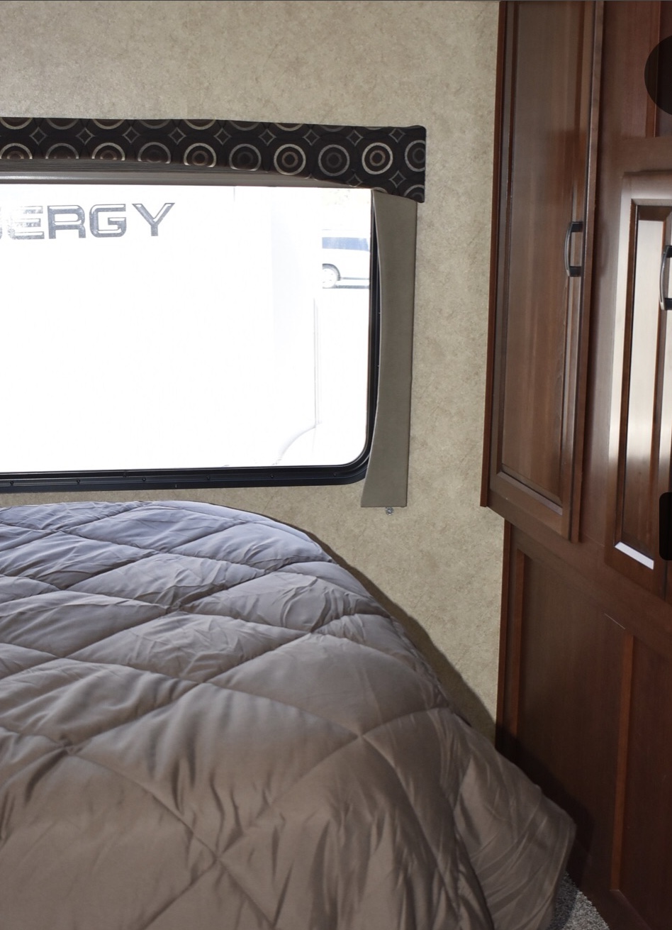 An RV rental bedroom with a cozy quilted bed, patterned valance over a large window, and wooden storage.. Forest River Forester Motorhome 2014