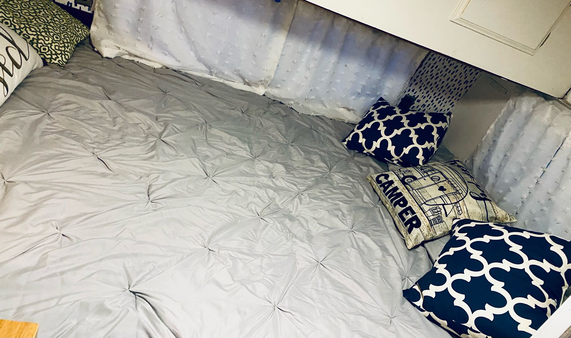 Cozy RV rental sleeping area with grey quilted bedding and decorative pillows, offering a comfortable and inviting space.. Coachmen Cadet 1977