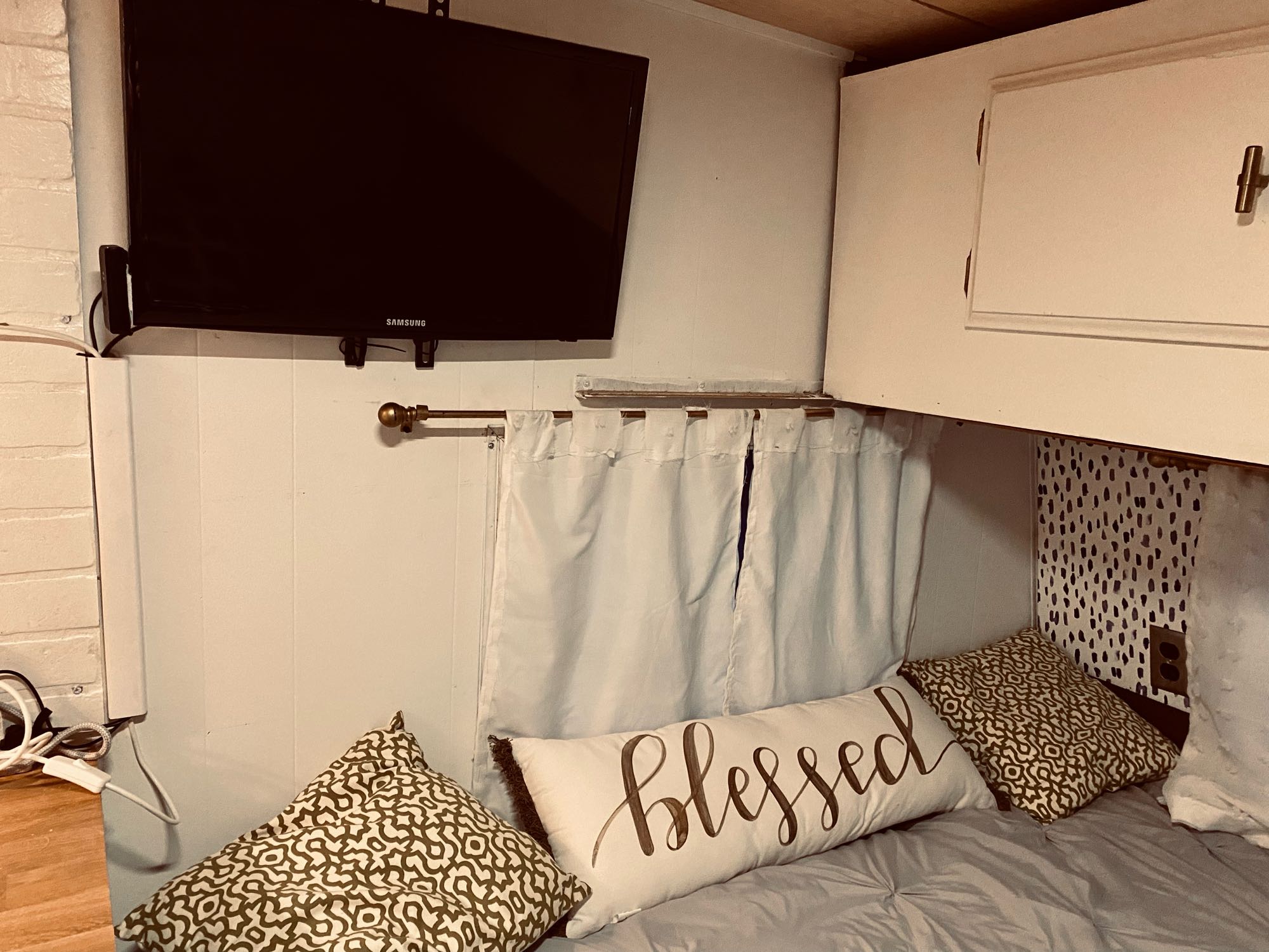 Relaxing RV rental interior featuring a mounted TV, quaint curtains, and a cozy bed with decorative pillows.. Coachmen Cadet 1977