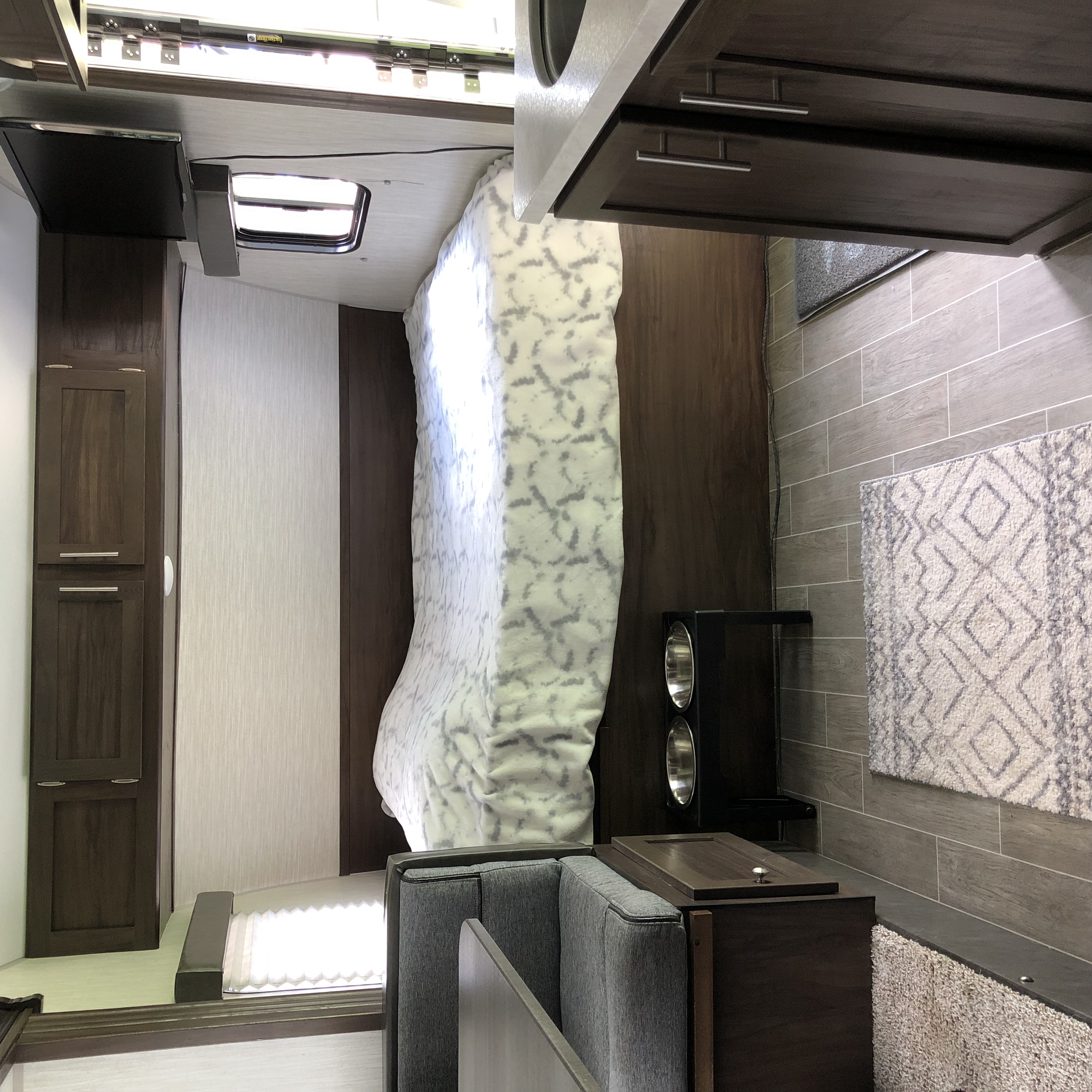 Modern RV rental interior: A cozy bedroom with a patterned bed, a living area with a sofa, and sleek wood-look cabinets. Ideal for travel.. Forest River Cherokee Wolf Pup 2020