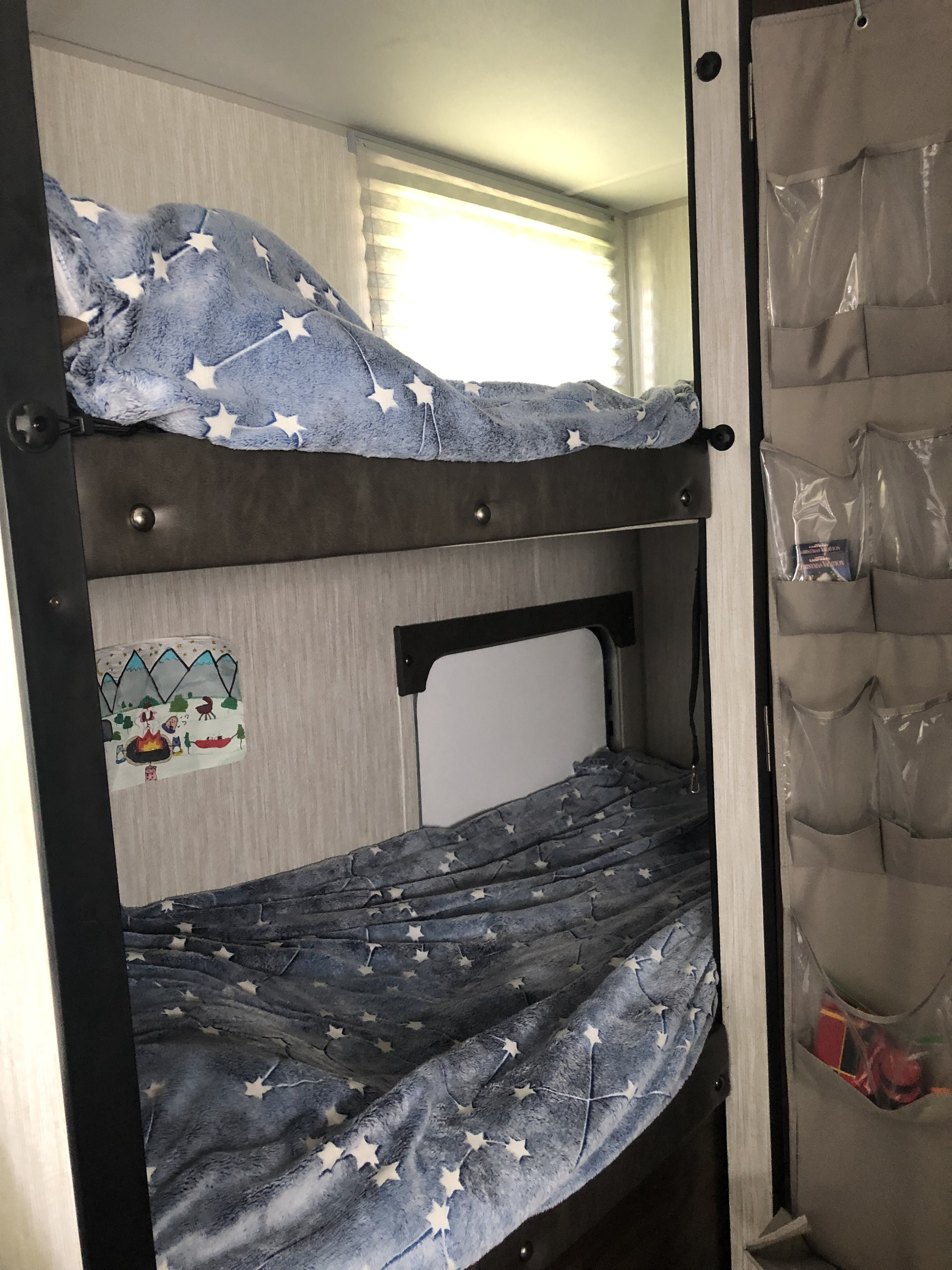 Cozy RV rental bunk beds with star-patterned blankets, a window, and storage organizer, perfect for family adventures.. Forest River Cherokee Wolf Pup 2020