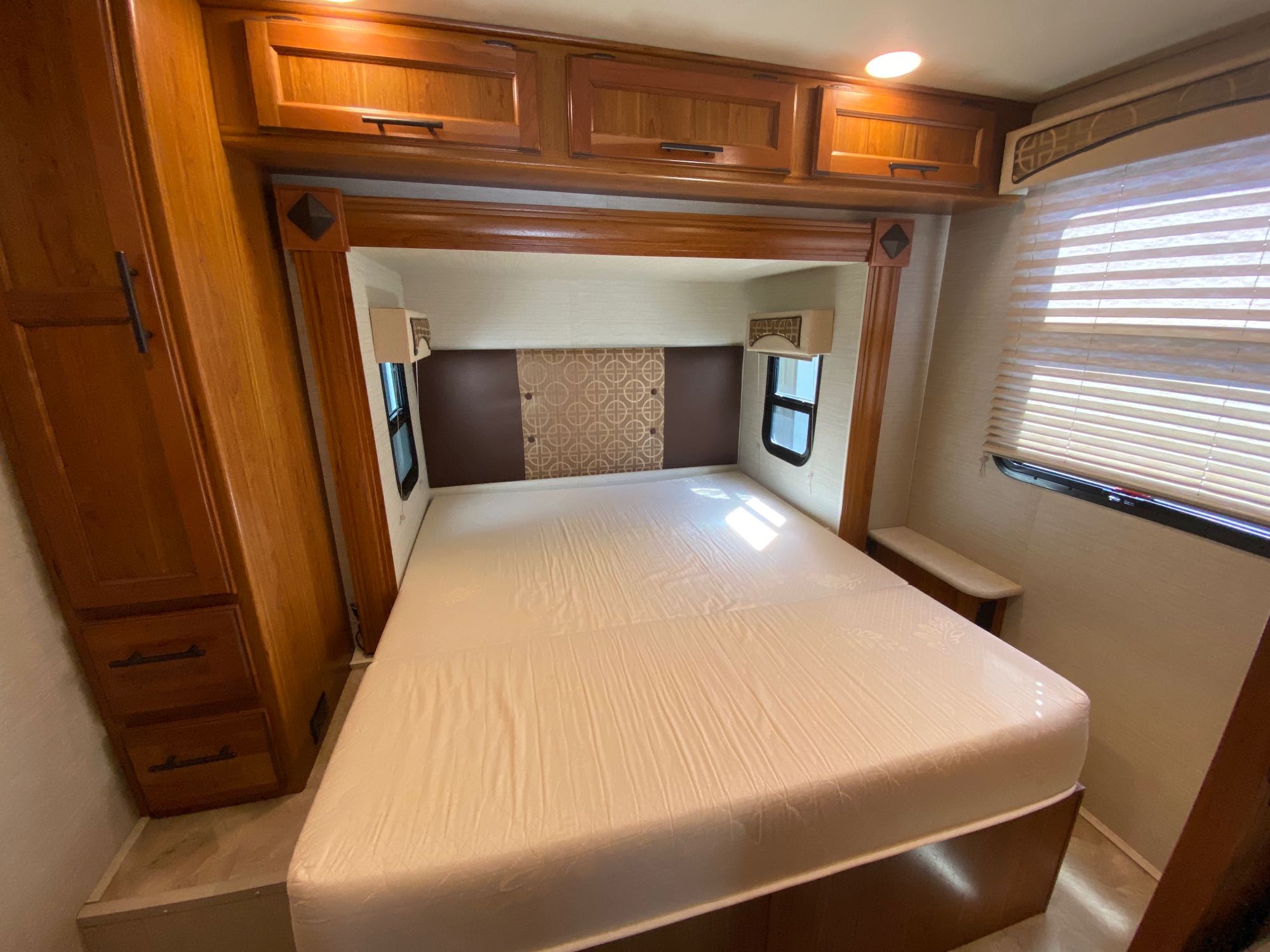RV rental bedroom: a comfortable bed with a decorative headboard, wood cabinets, and a bright window. Your travel retreat.. Jayco Melbourne 2017