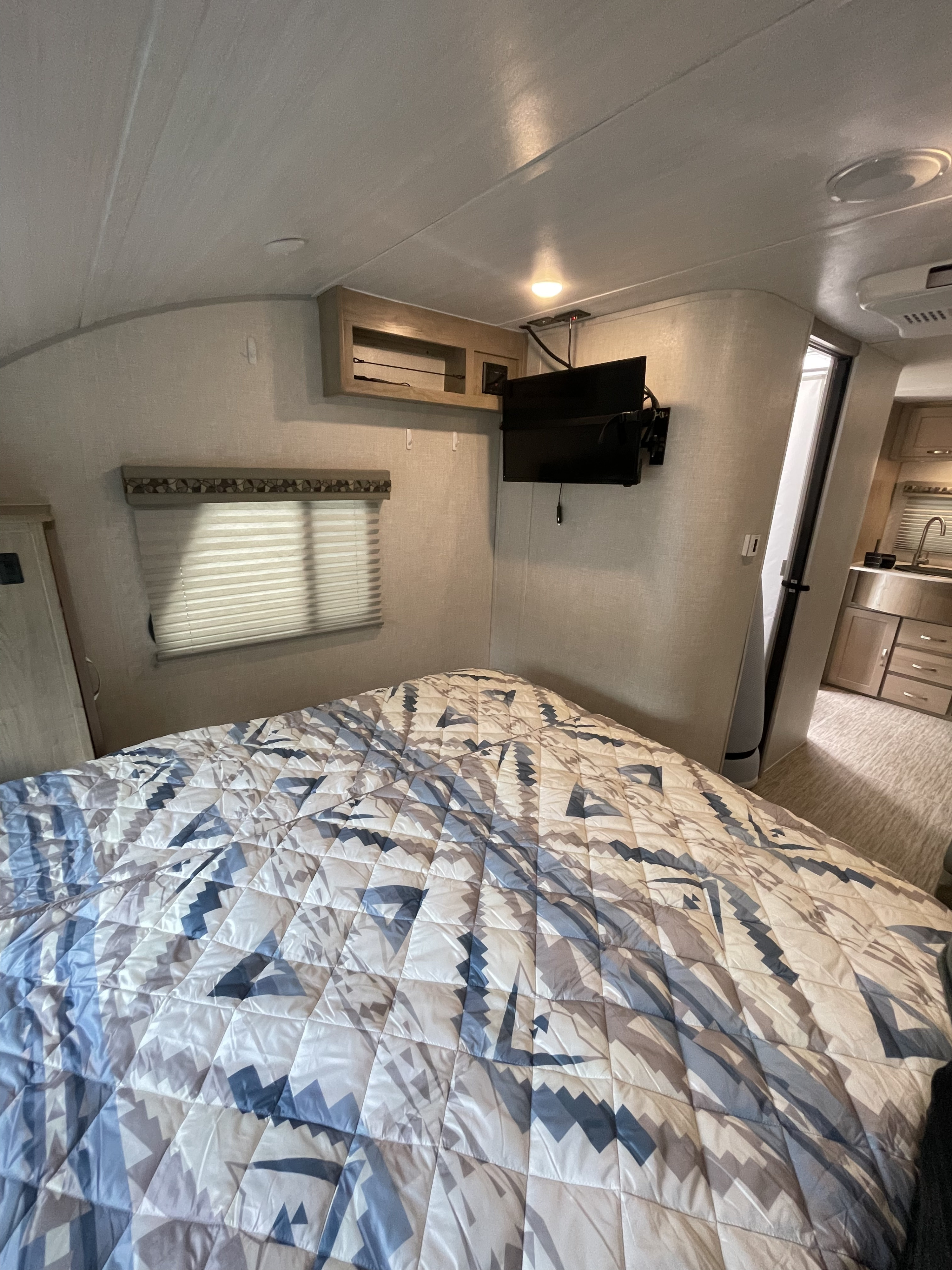 This comfortable RV rental bedroom features a patterned bed, wall-mounted TV, and window, perfect for your travel adventures.. R-Pod Hood River Edition 2020