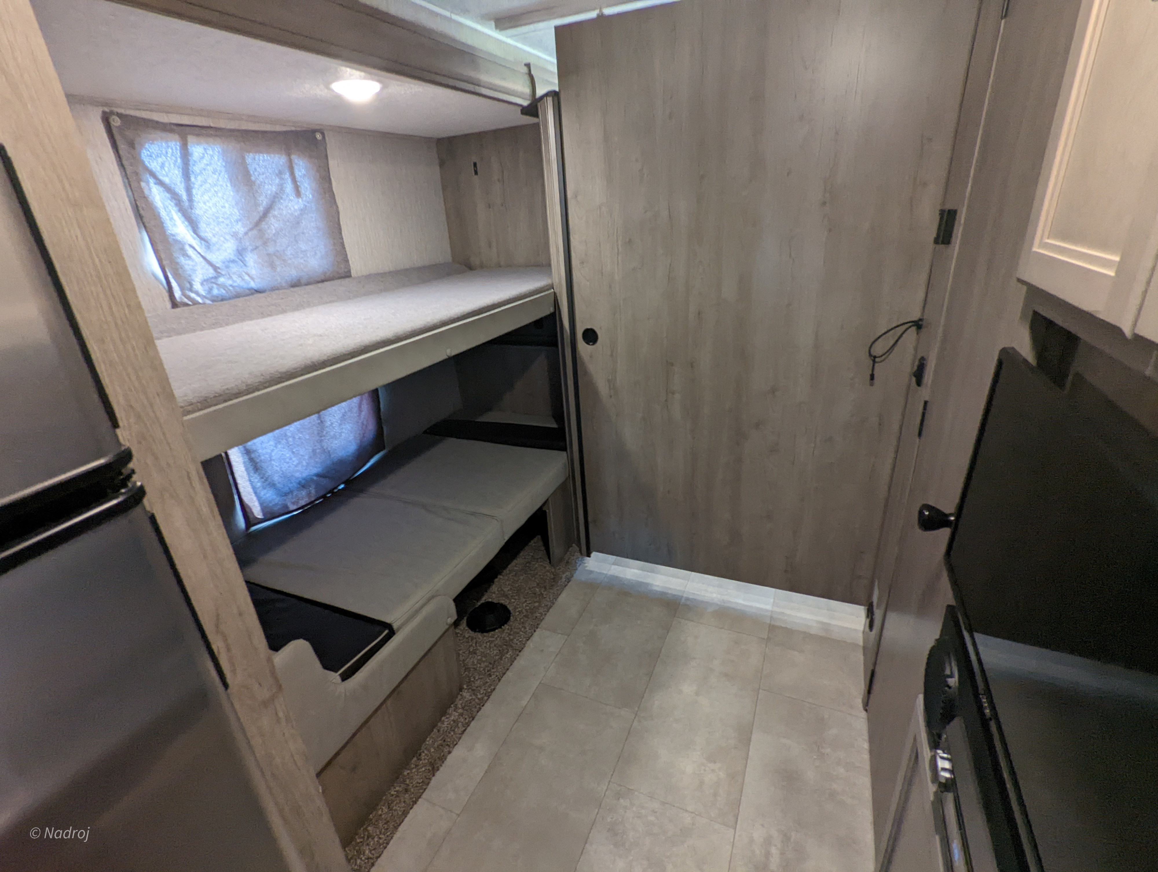 RV rental interior: two-tier bunk beds, adjacent refrigerator, and compact living area with a door and wall-mounted TV.. Forest River Coachmen Freelander Premier 2021