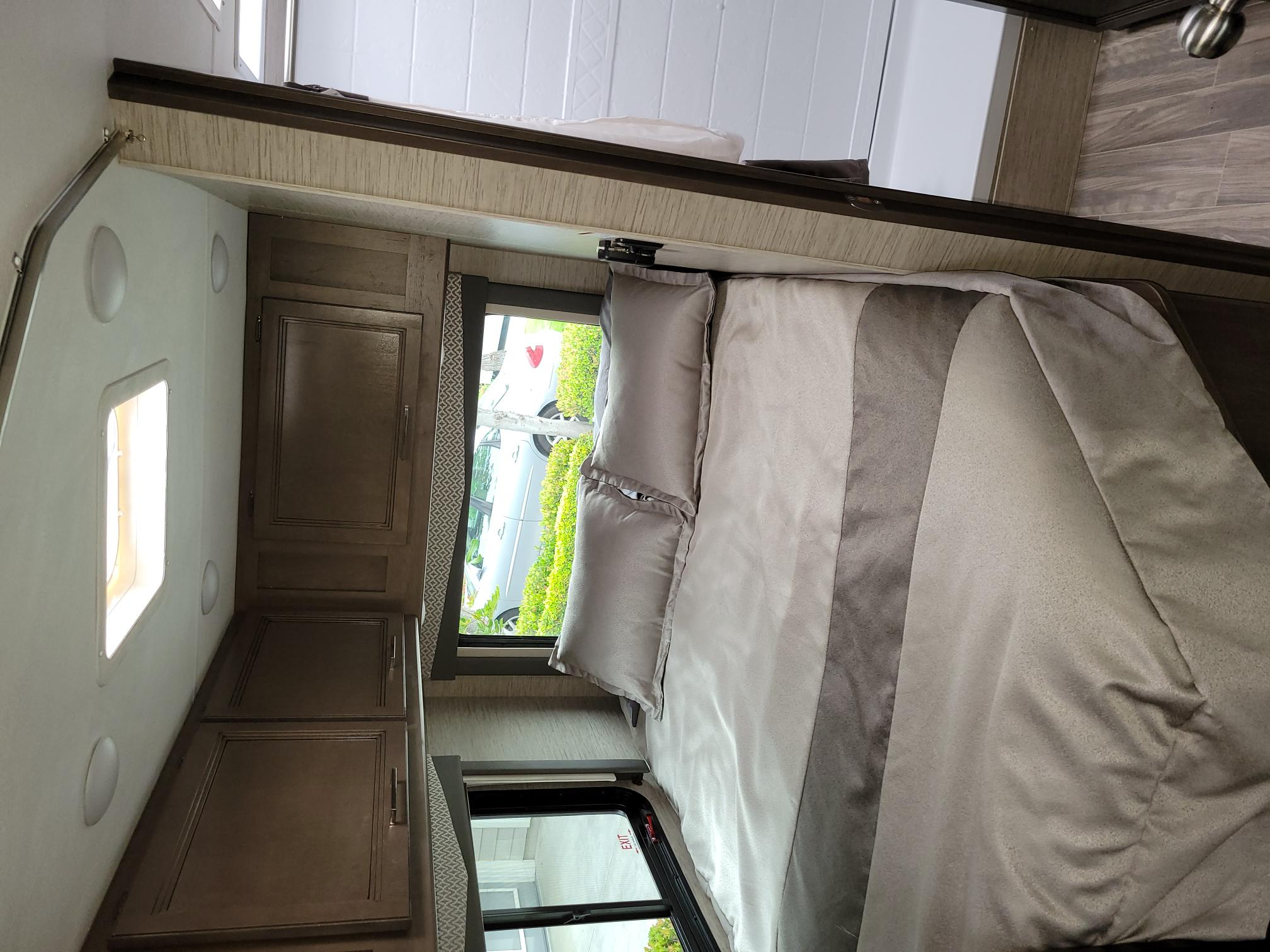 RV rental bedroom: a clean, inviting space with a neutral gray bed, wood cabinets, and two bright windows.. Thor Four Winds 2022