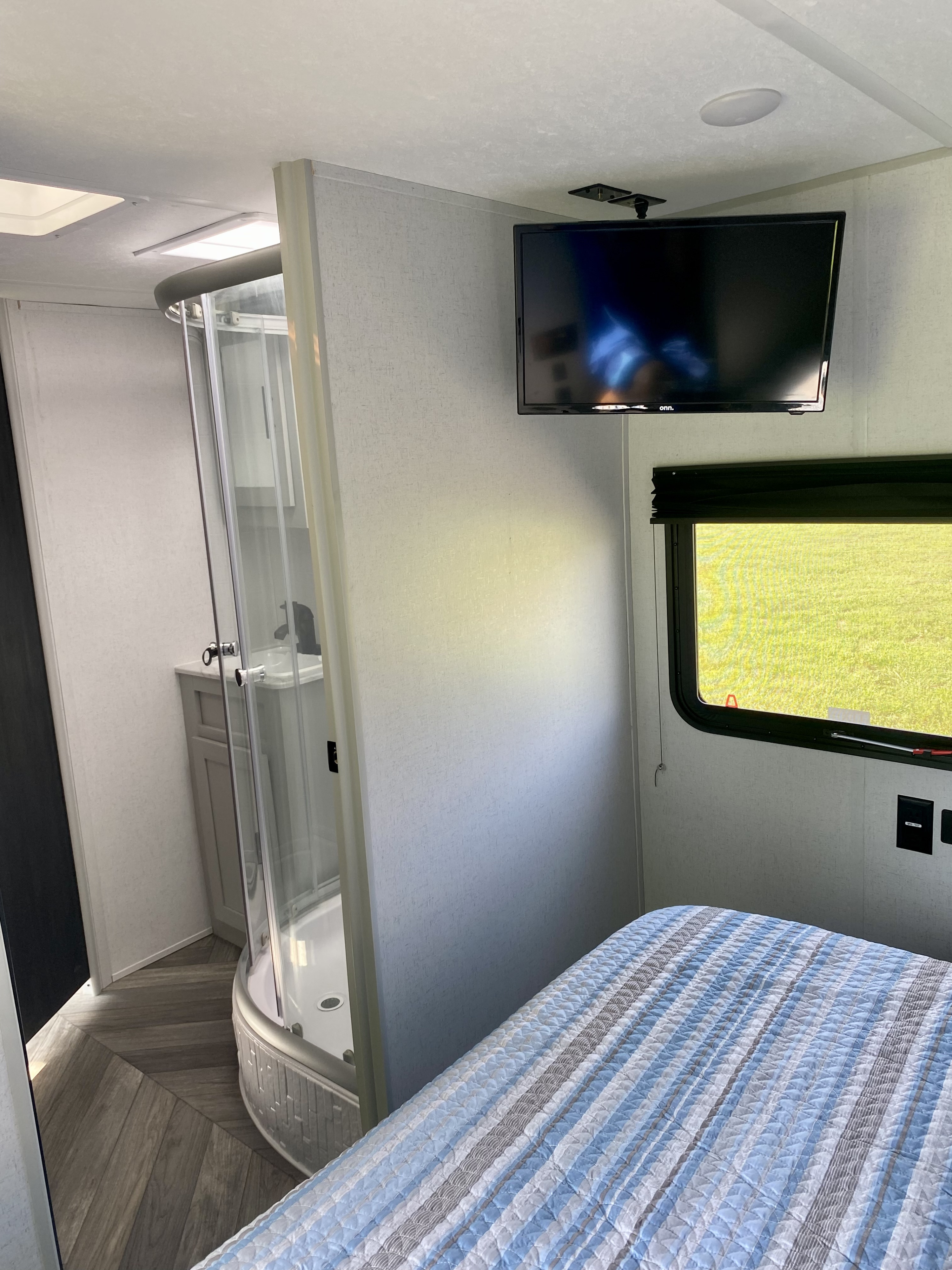 Cozy RV rental bedroom features a striped bed, TV, window, and a compact glass shower enclosure for convenient living.. Forest River Salem 2022