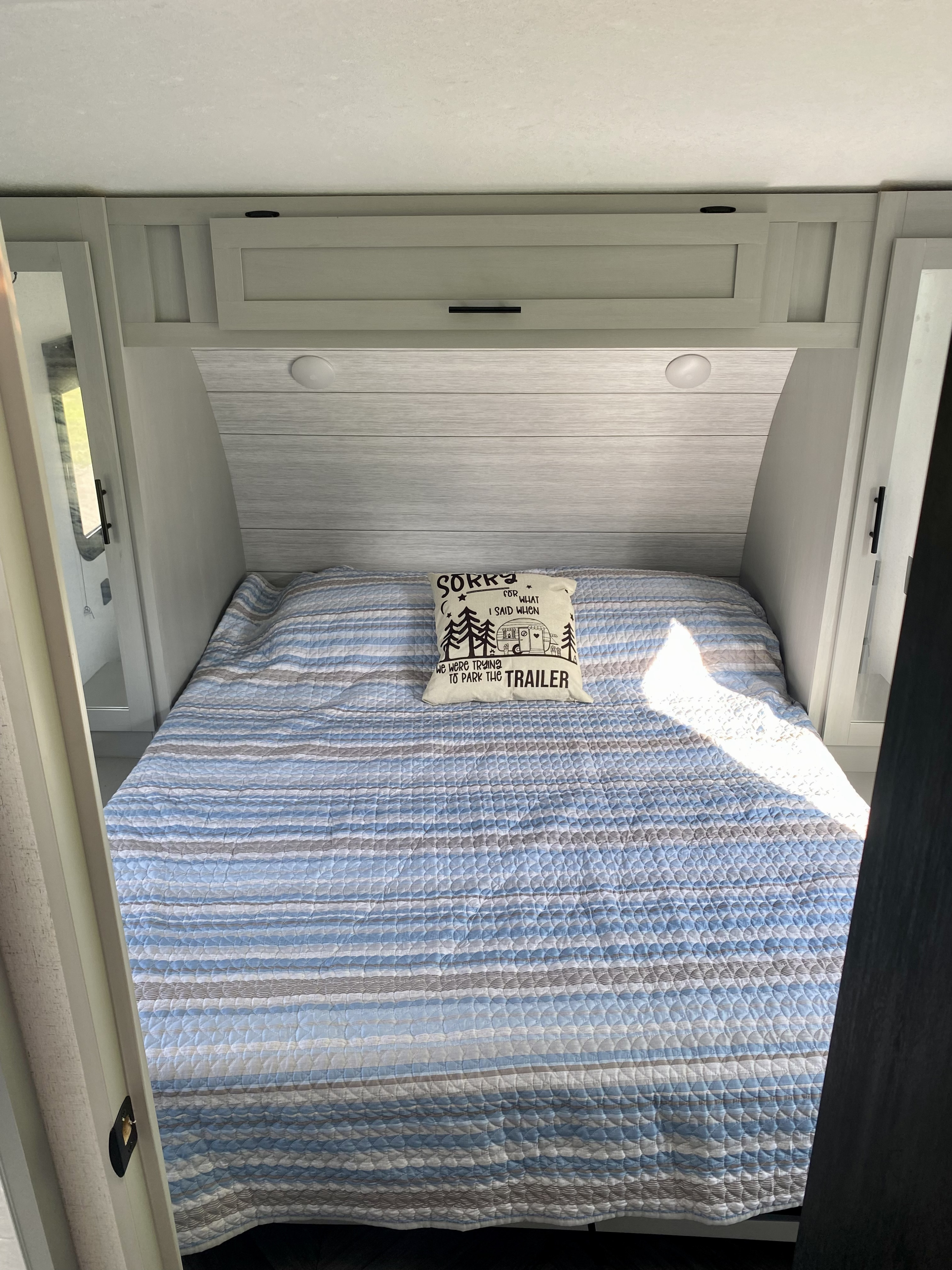 Cozy RV rental bedroom featuring a blue and grey quilted bedspread, a humorous "trailer parking" pillow, and bright light.. Forest River Salem 2022