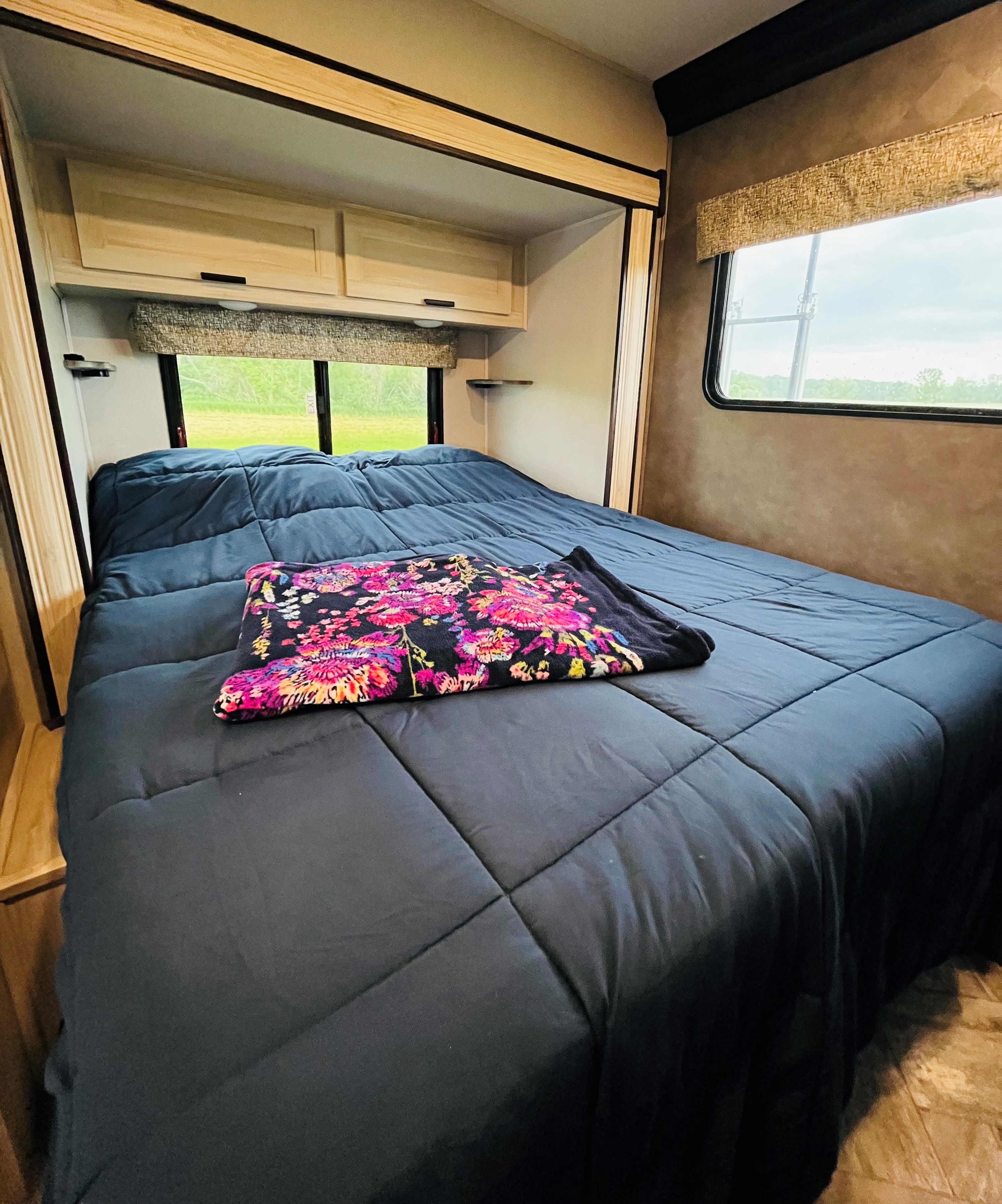 Inviting RV rental bedroom with a dark blue comforter, vibrant floral throw, overhead storage, and scenic windows.. Forester LE 2021