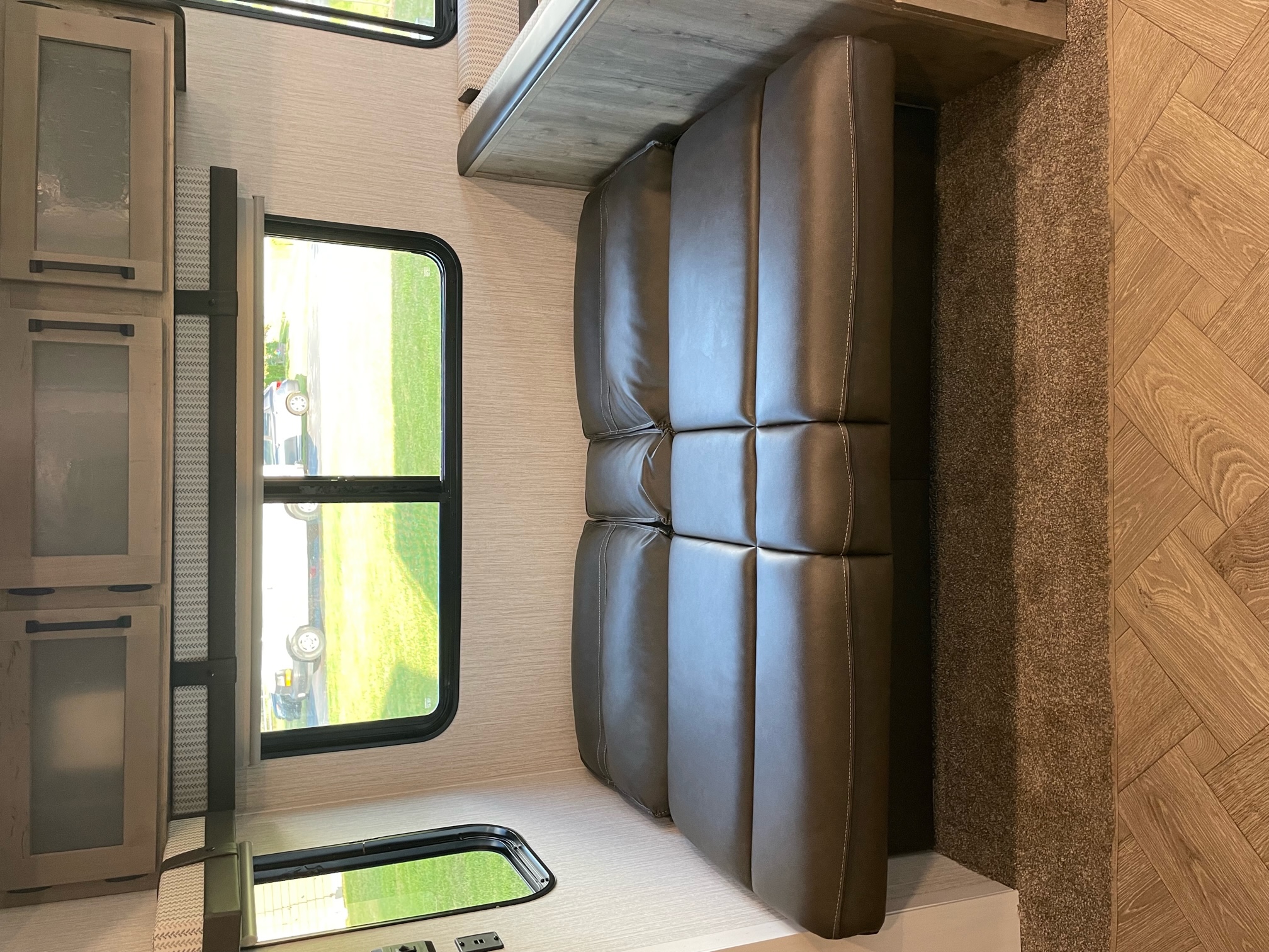 RV rental interior: A cozy brown sofa with a wood shelf above, light wood cabinets, windows with a view, and mixed flooring.. Forest River Palomino Puma 2021
