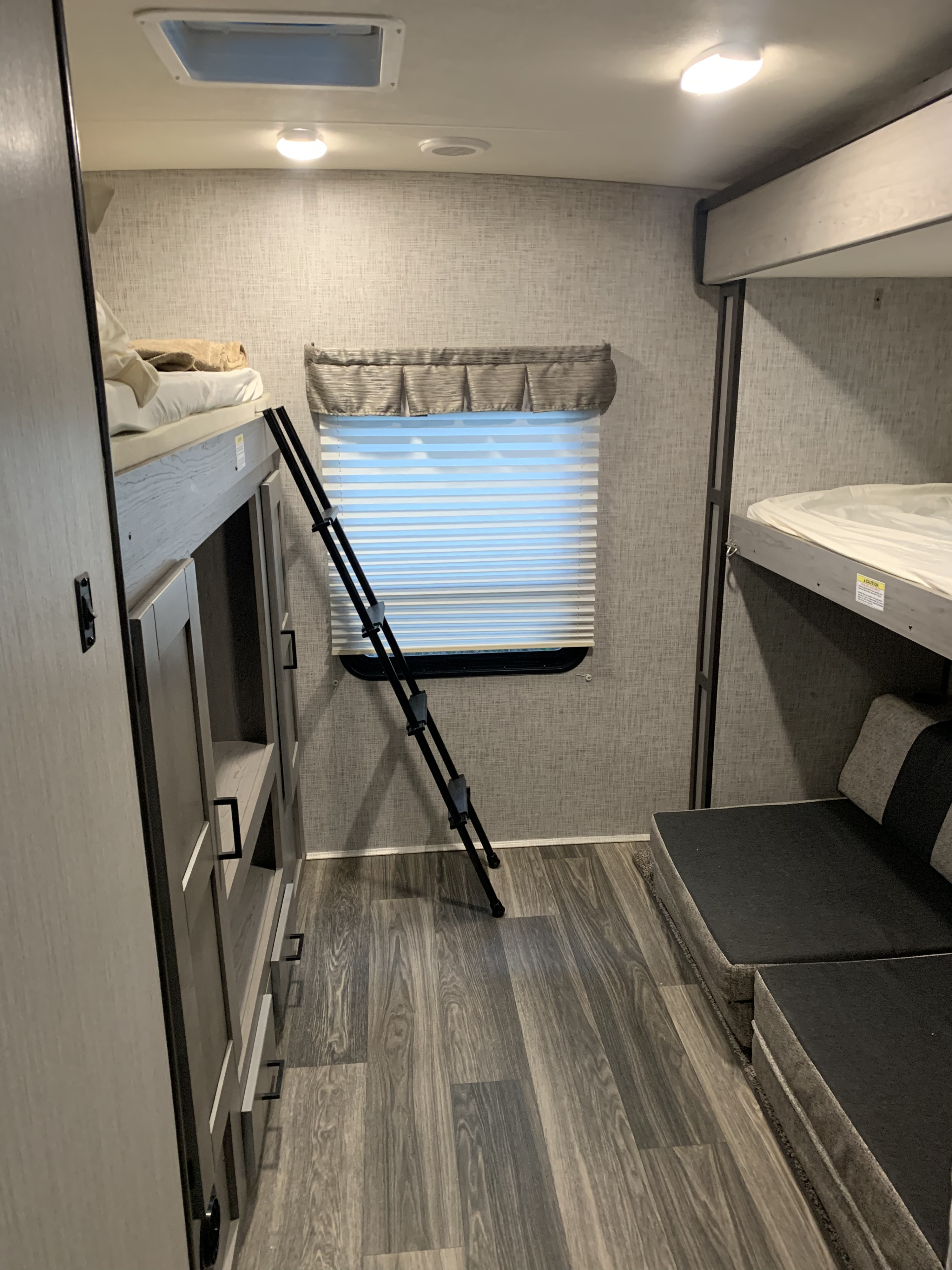 Inside an RV rental, showing bunk beds on both sides with a ladder, window, and seating for comfortable travel.. Heartland RVs Mallard 2021