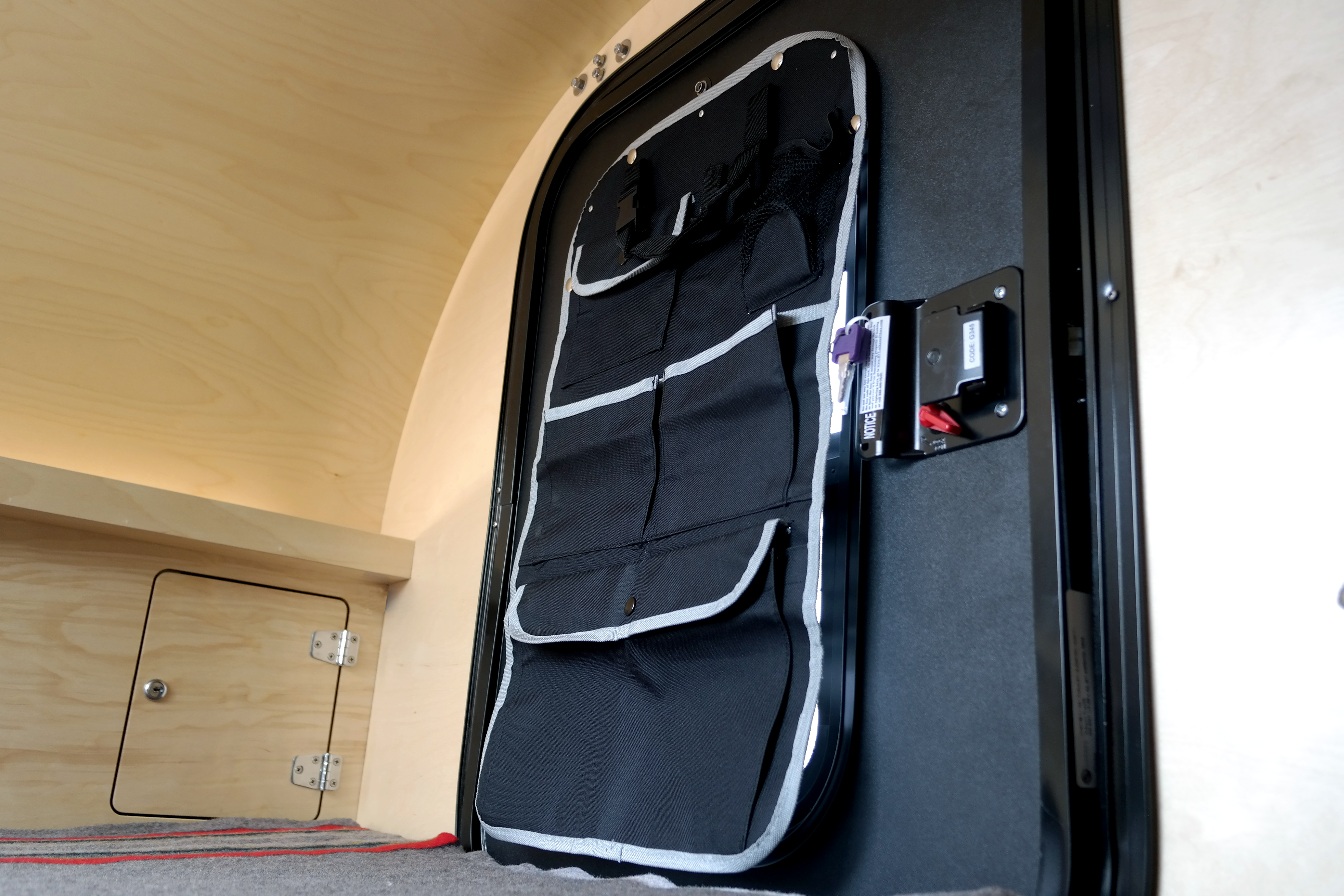Inside an RV rental: A door-mounted organizer adds storage to the black door, with light wooden walls and a storage hatch.. Oregon Trail'R DoDrop 2022