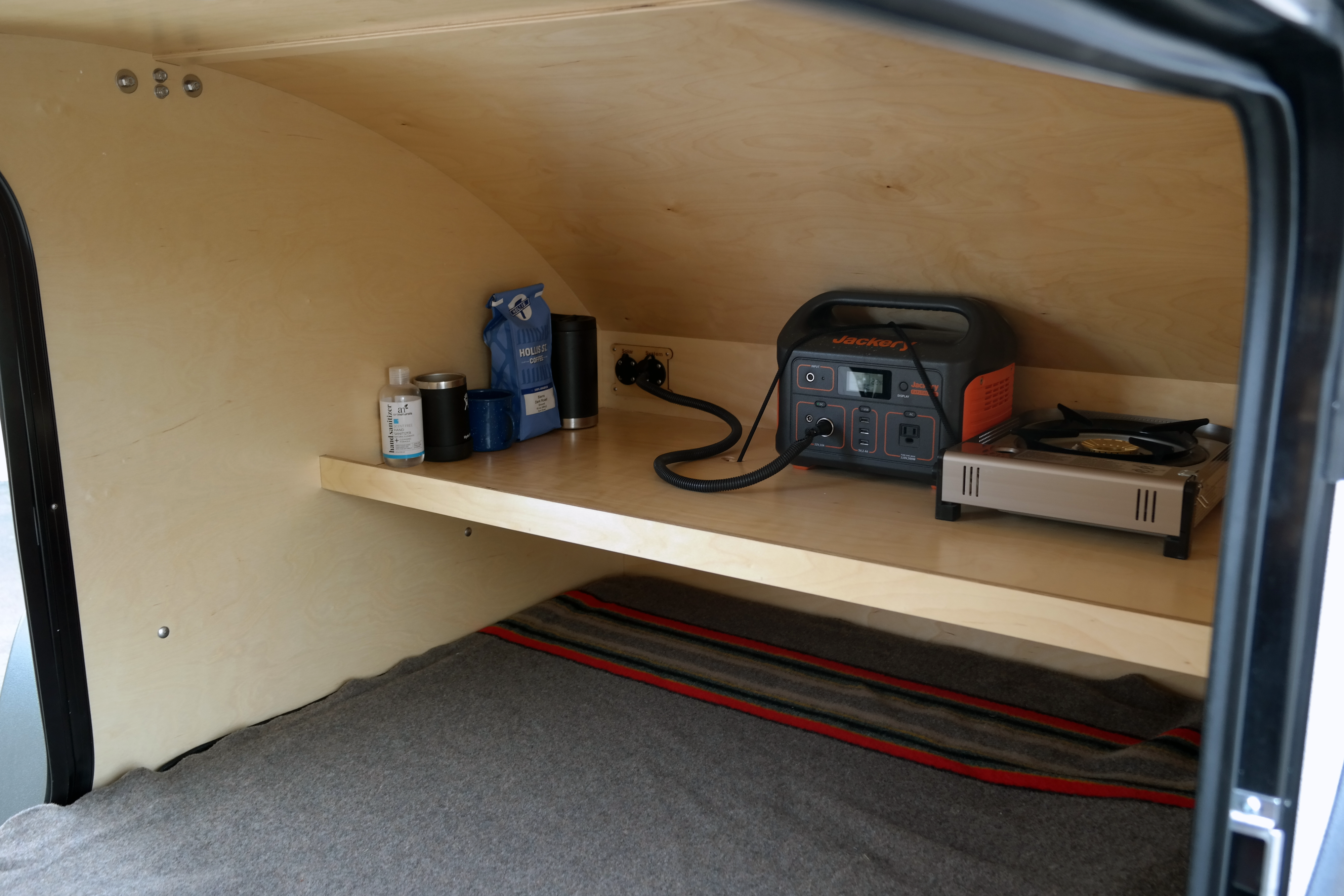 Inside a cozy RV rental: a shelf with a Jackery power station, portable stove, coffee, and bedding below.. Oregon Trail'R DoDrop 2022