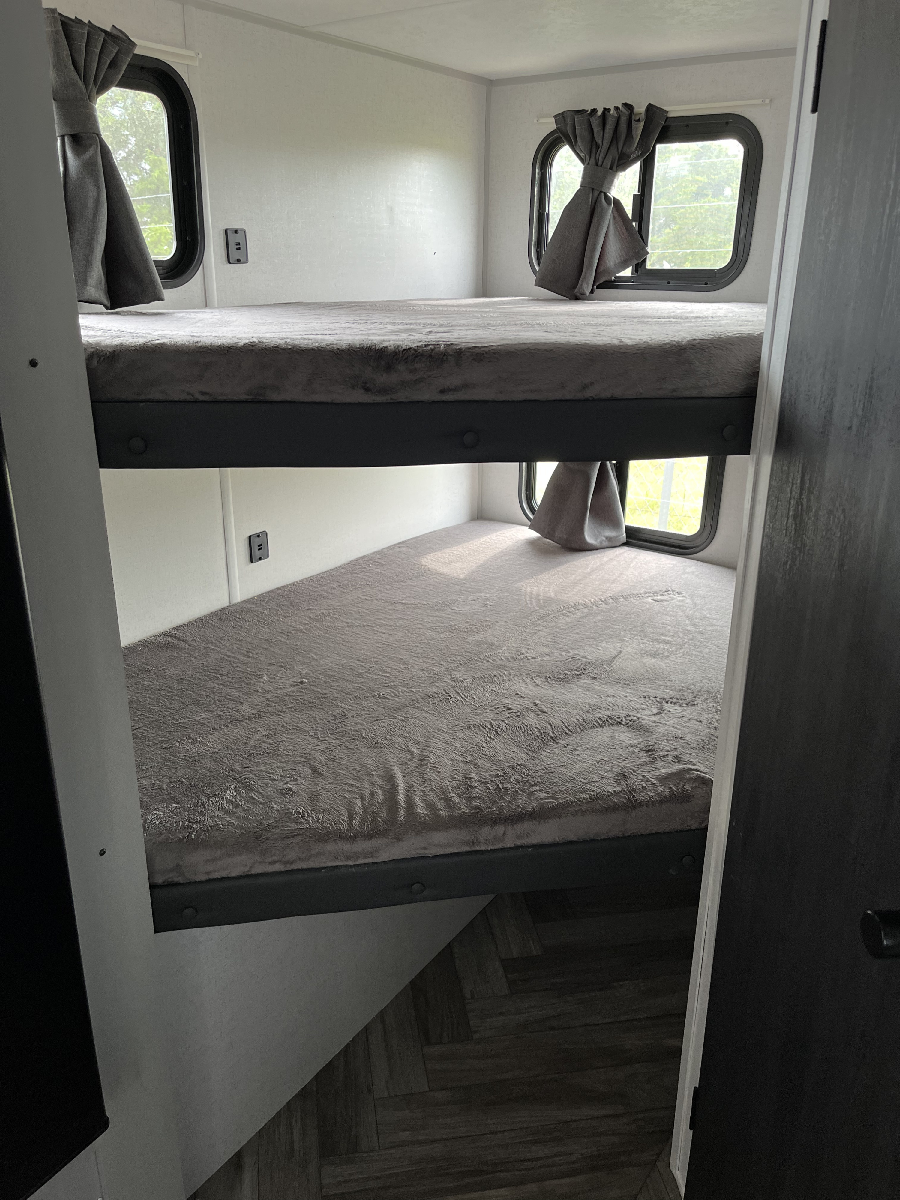 Cozy RV rental interior: stacked bunk beds with plush grey bedding and windows with curtains, ideal for sleeping.. Forest River Wildwood FSX 2022