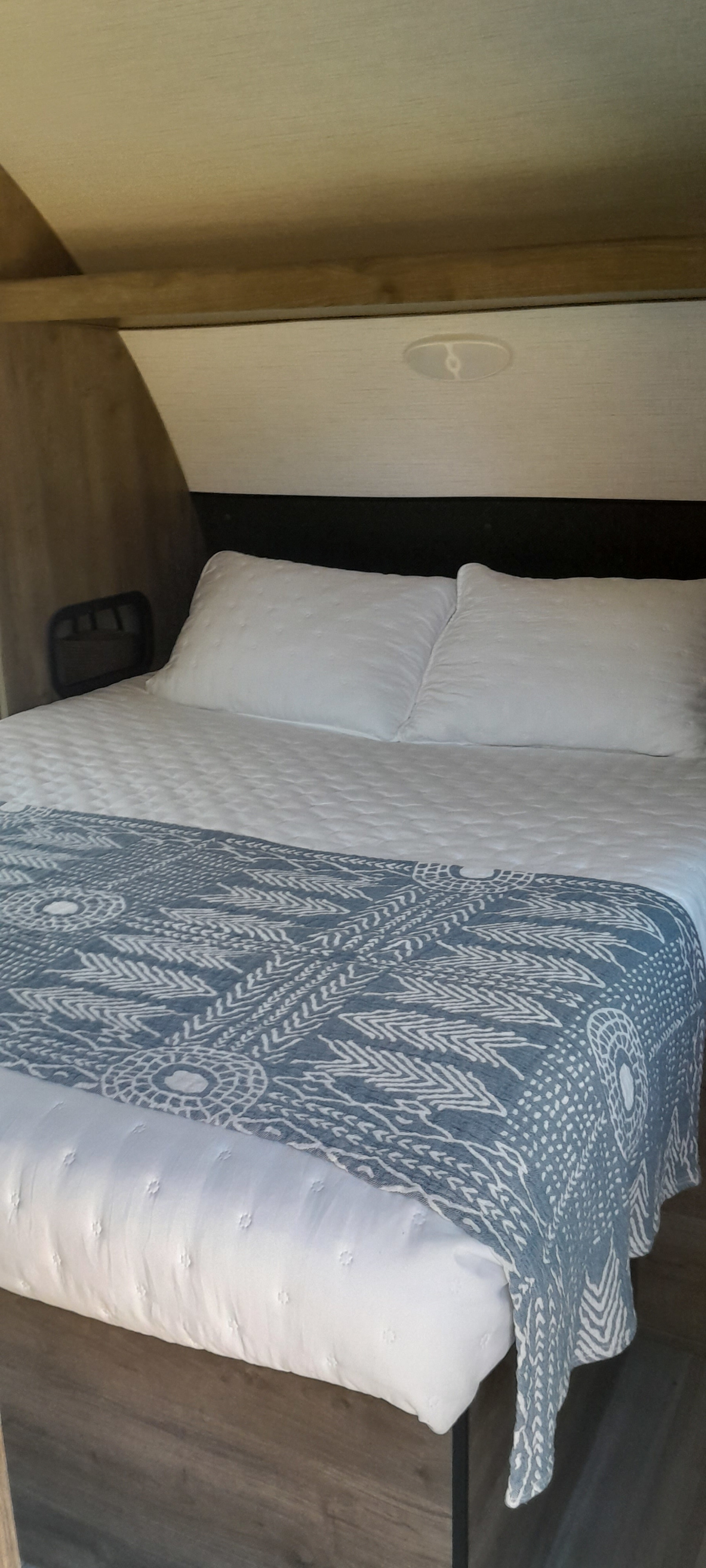 Clean, cozy bed setup in an RV rental, with white quilted bedding and a decorative blue blanket. Ready for a relaxing trip.. Heartland Pioneer BH280 2022