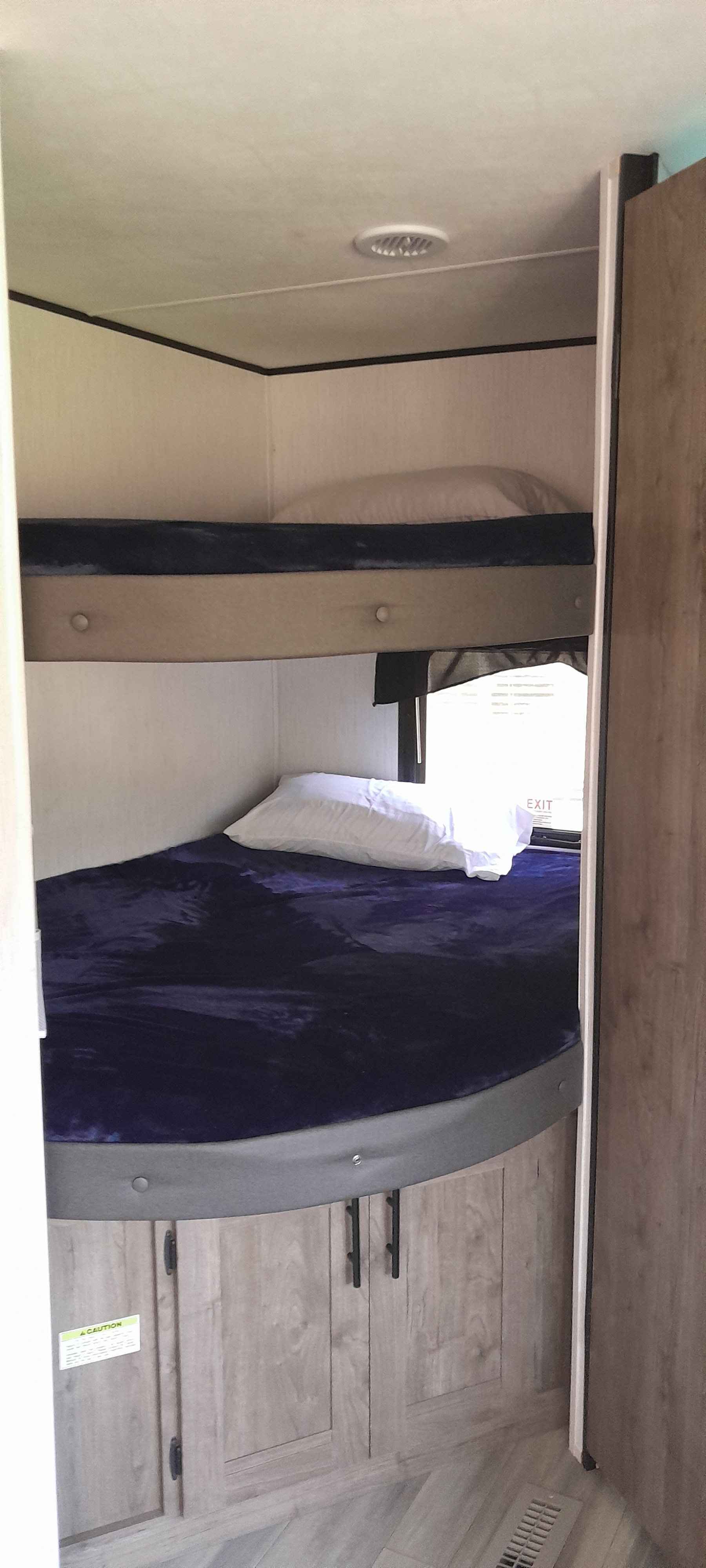 Compact RV rental sleeping area with two bunk beds, white pillows, a dark blue blanket, and wood cabinetry.. Heartland Pioneer BH280 2022