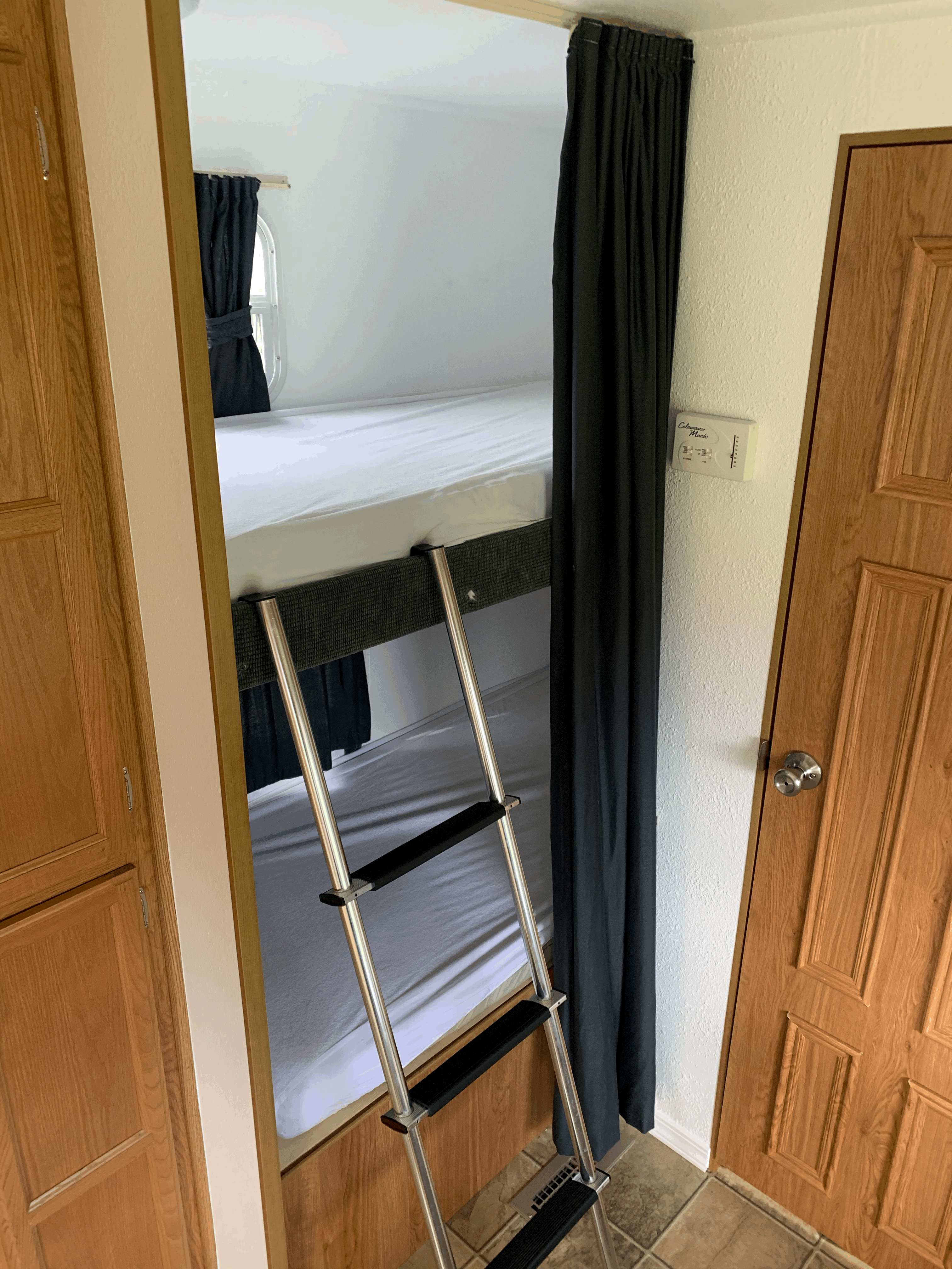 RV rental interior: a bunk bed with ladder, dark curtains, wood cabinetry, and thermostat, ideal for comfortable sleeping.. Jayco Jay Flight 2007