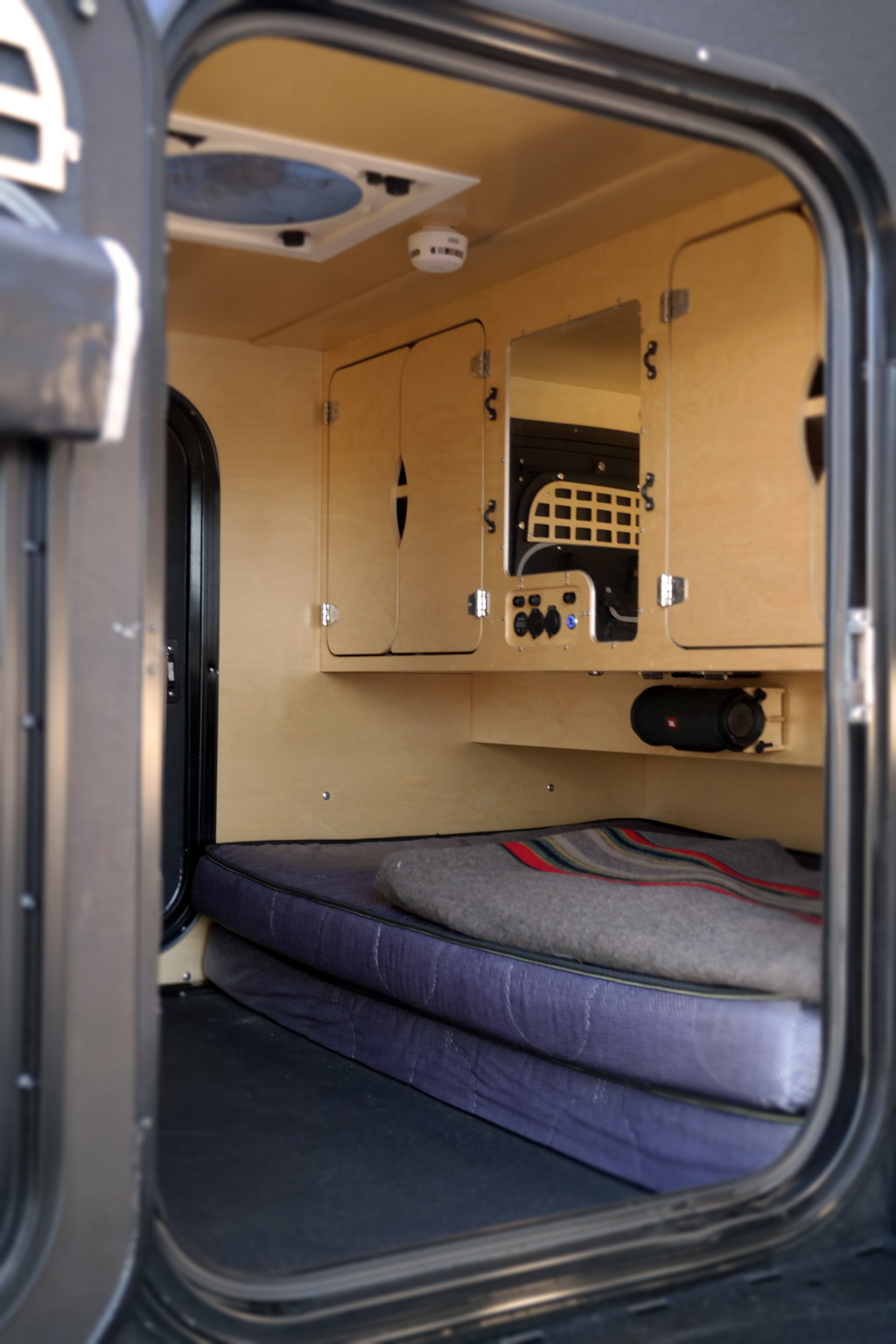 Compact RV rental interior: cozy bed, wood cabinetry, fan, and controls, ready for mobile adventures.. Oregon Trail'R TerraDrop ALPHA 2022