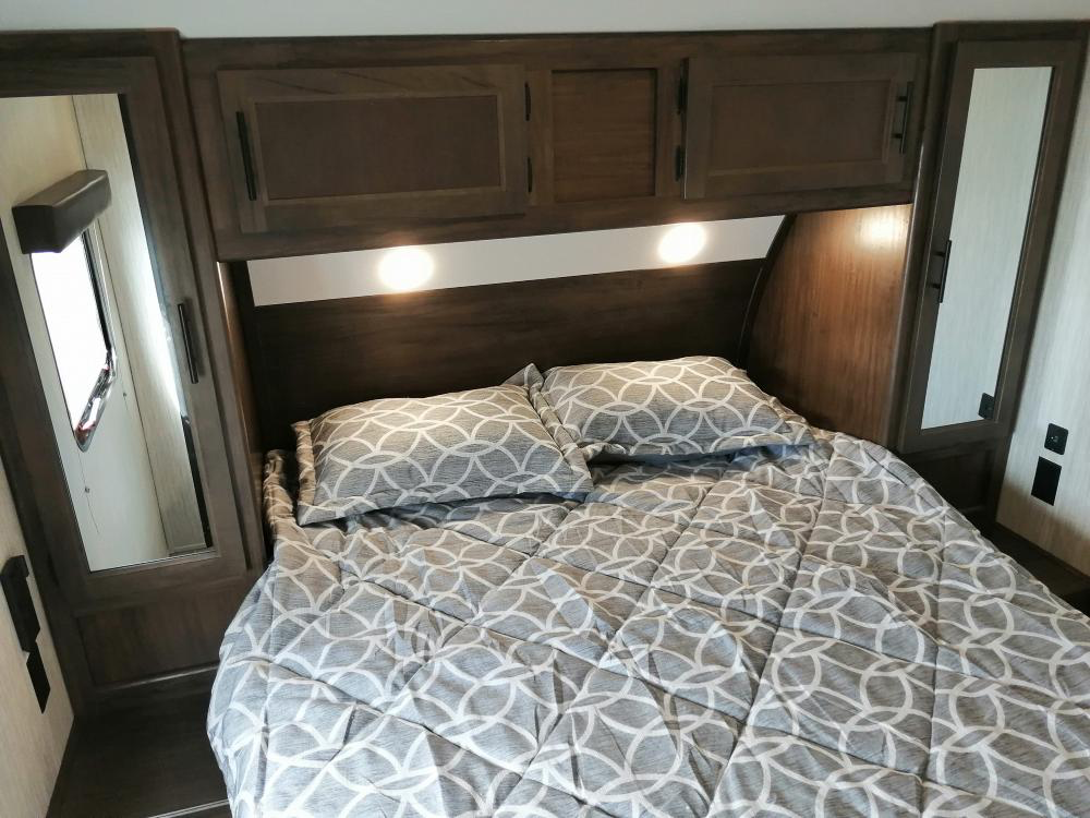 Cozy RV rental bedroom with patterned bed, dark wood overhead cabinets, bright reading lights, and mirrored wardrobes for comfortable travel.. Forest River Cherokee Grey Wolf 2020