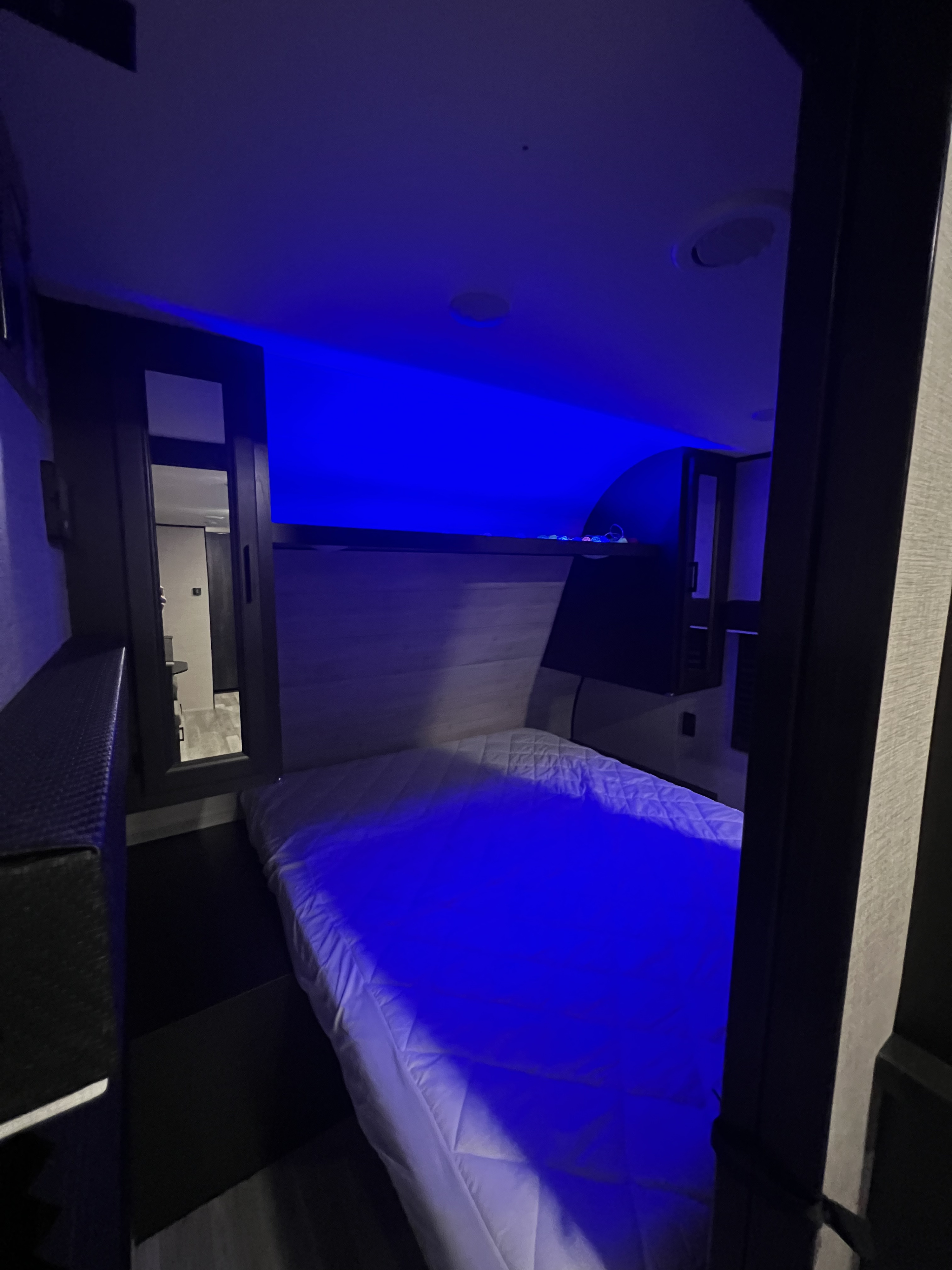 RV rental interior: A cozy bedroom with a white mattress, bathed in blue LED lights, glimpsing another area.. Jayco Jay Flight SLX 2022