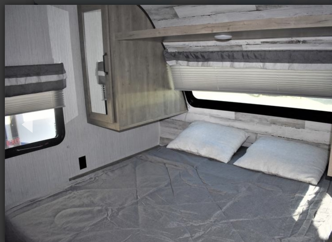 Cozy RV rental bedroom featuring a bed with gray bedding, two pillows, window with blinds, and light wood cabinetry.. Palomino XLE lite 2022