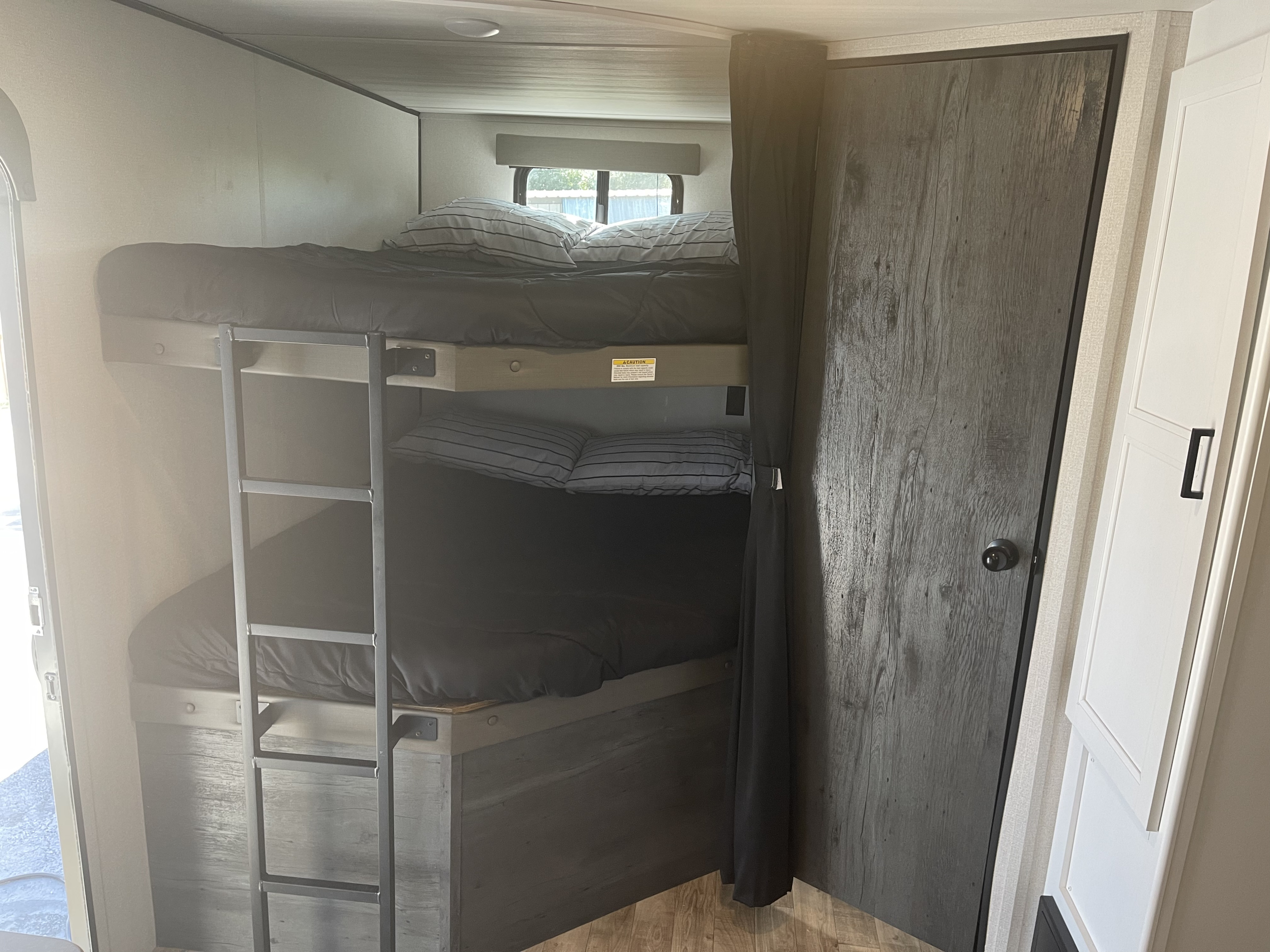 Inside an RV rental: Two bunk beds with black bedding and a ladder offer compact sleeping arrangements and privacy.. Keystone RV Hideout 2022