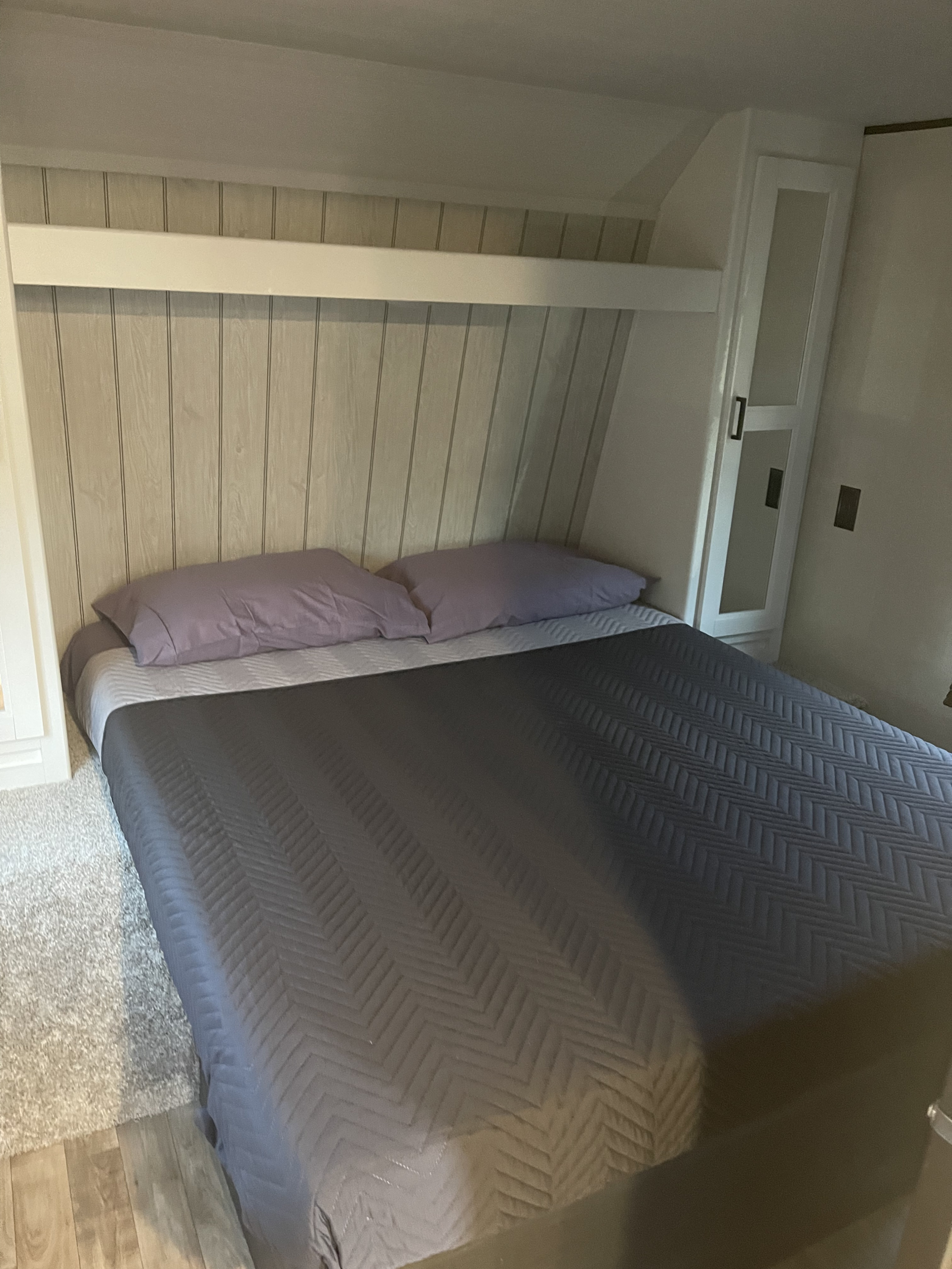 Cozy RV rental bedroom featuring a bed with purple pillows, modern paneled headboard, and built-in storage cabinets.. Keystone RV Hideout 2022