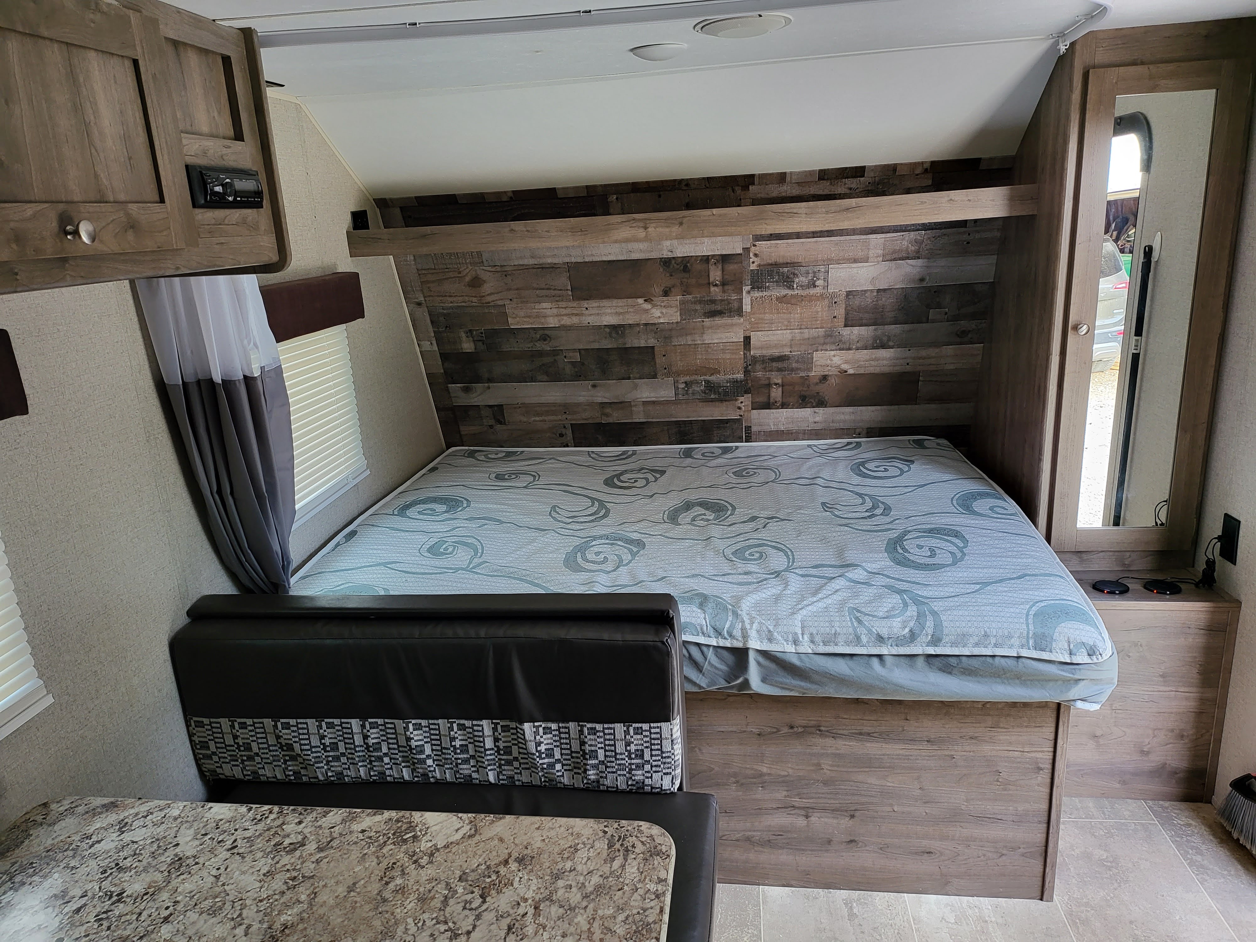 RV rental interior with a cozy bed, wood accent wall, built-in dinette, and storage for comfortable travel.. Aspen Trail LE 2020