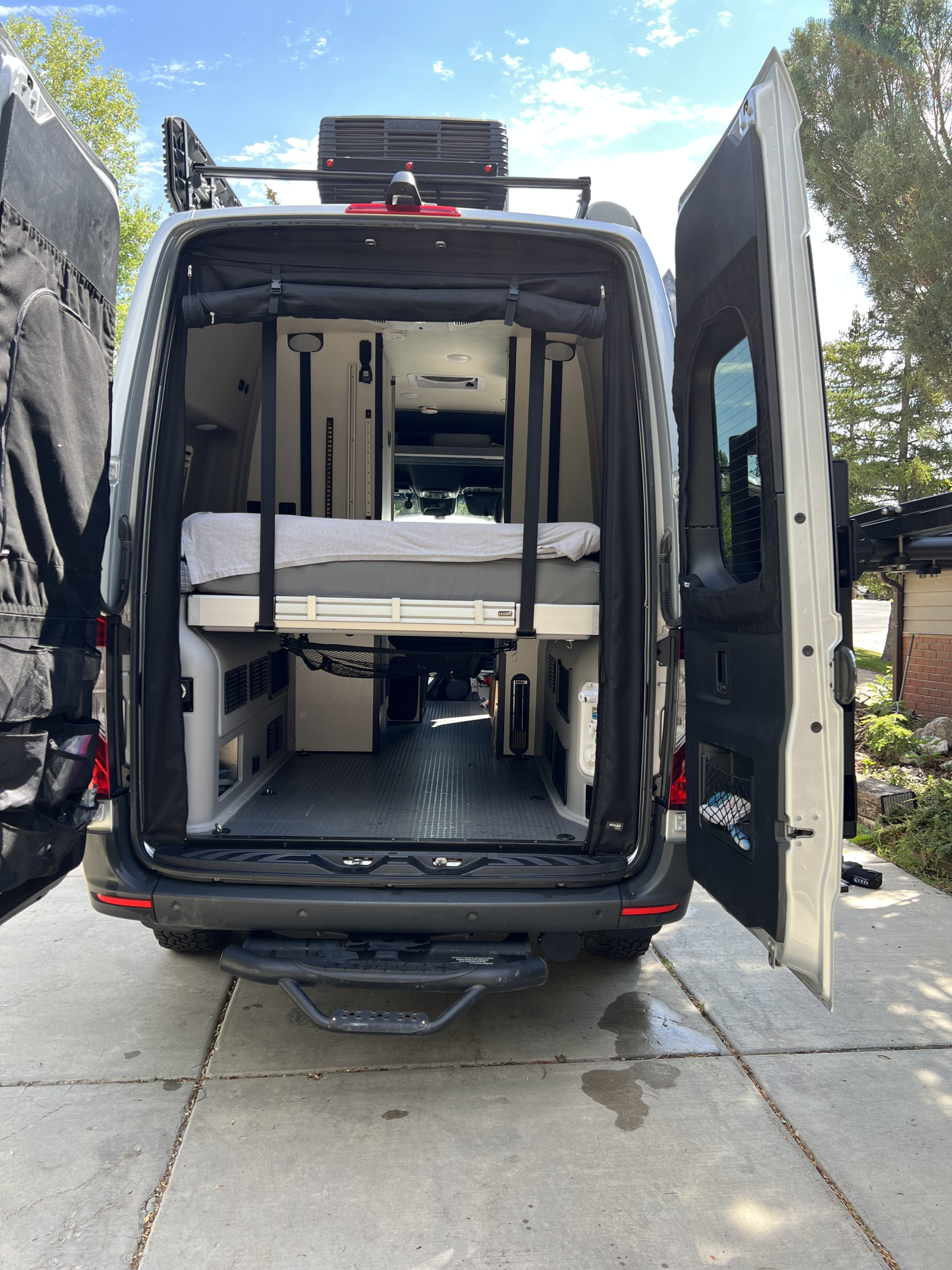 Open rear doors of an RV rental show a spacious interior with an elevated bed & storage for adventures.. Winnebago Revel 2022