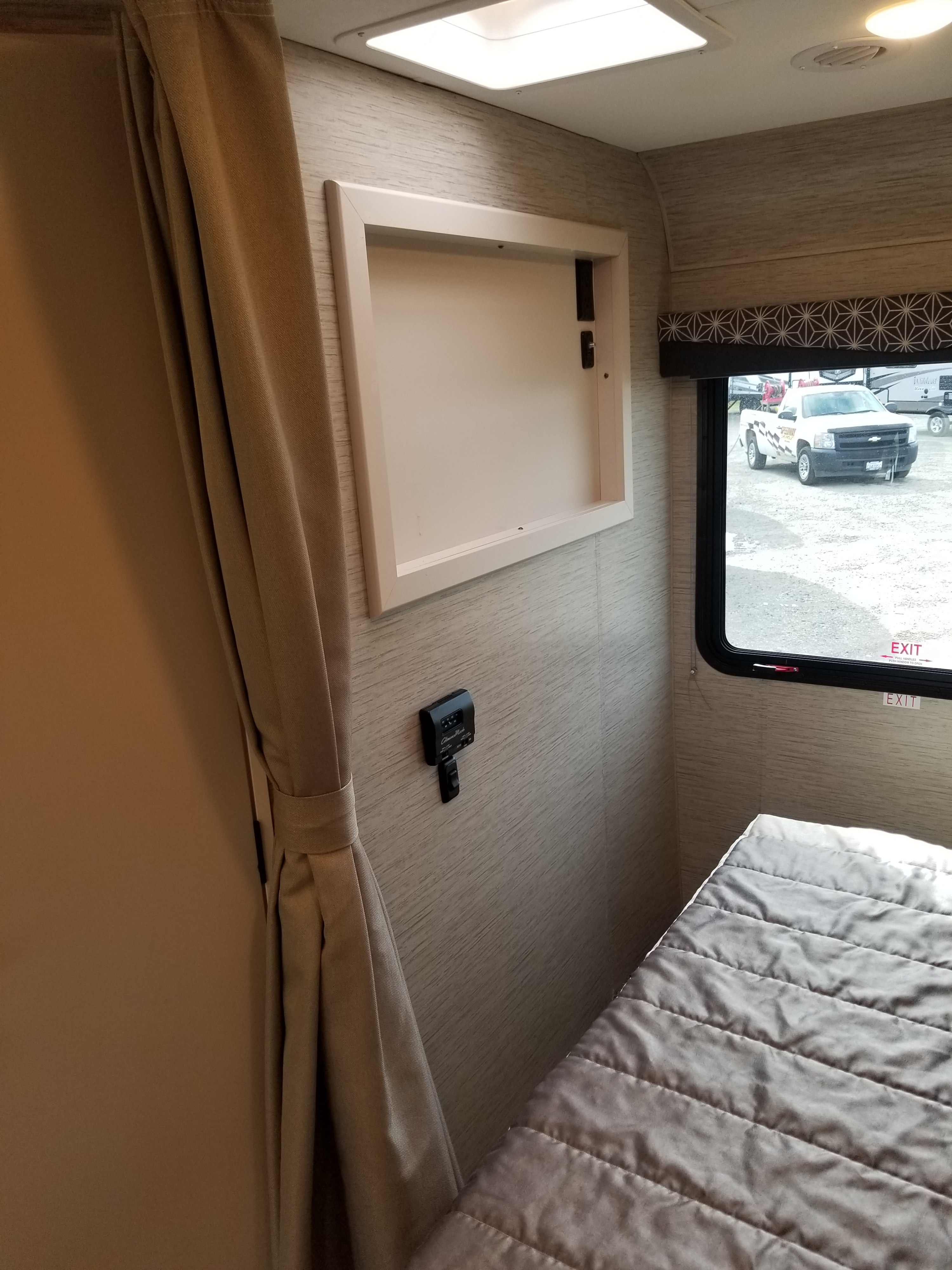 RV rental interior: a bedroom space with a grey bed, window, wall-mounted controls, and open storage.. Thor Motor Coach Freedom Elite 2022