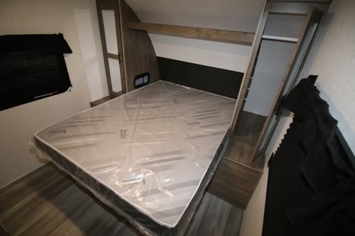 Clean RV rental bedroom featuring a new bed with plastic-wrapped mattress and built-in storage, ready for travel comfort.. Heartland RVs Pioneer 2022