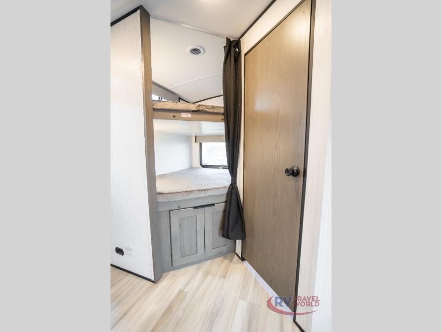 This RV rental features a compact bunk bed area and a wooden door, showcasing an efficient travel trailer interior.. Cruiser RV MPG Ultra Lite 2022