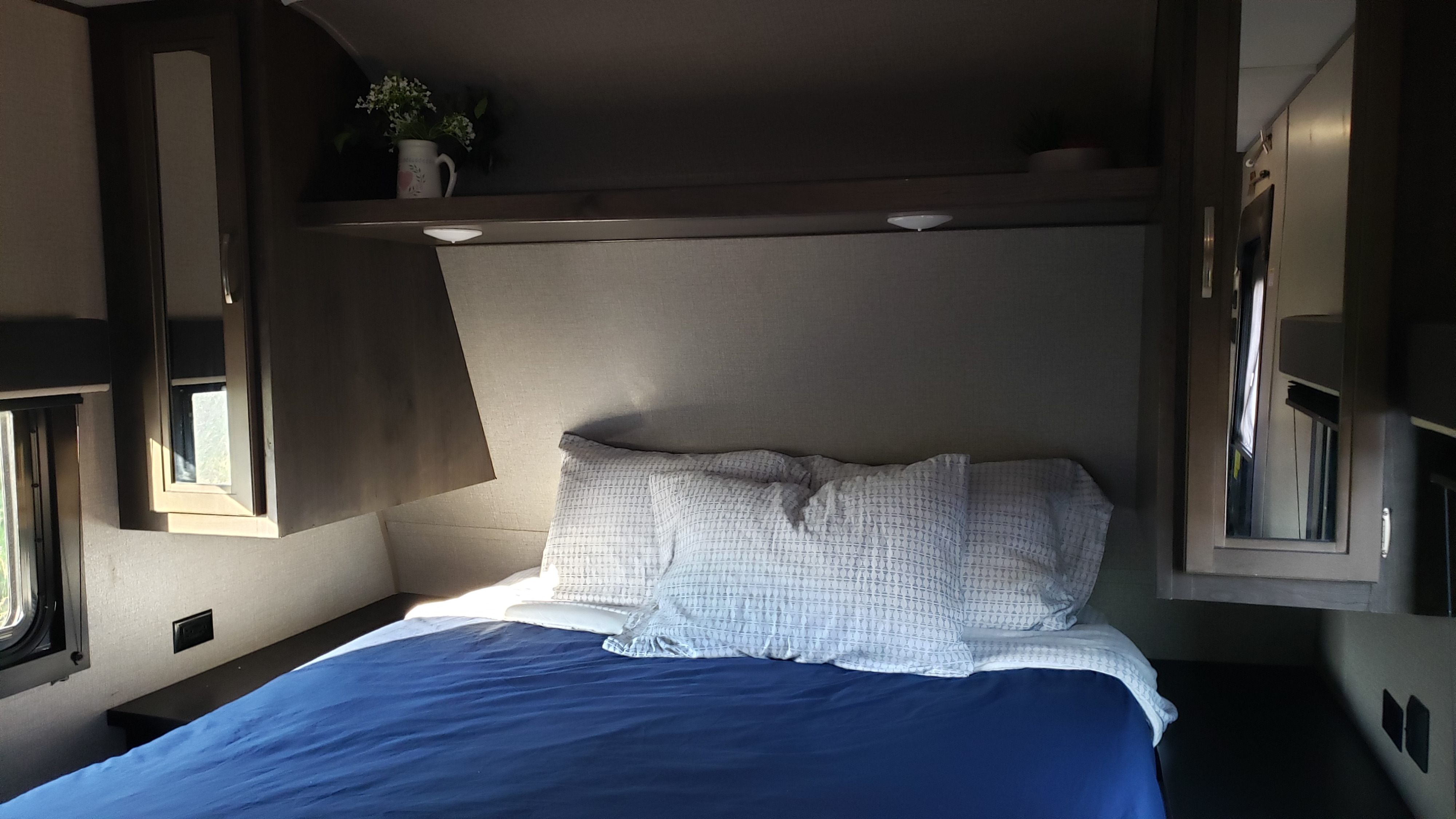 Interior view of an RV rental bedroom with a neatly made bed, overhead cabinets, and small windows for natural light.. Jayco Jay Flight SLX 2019