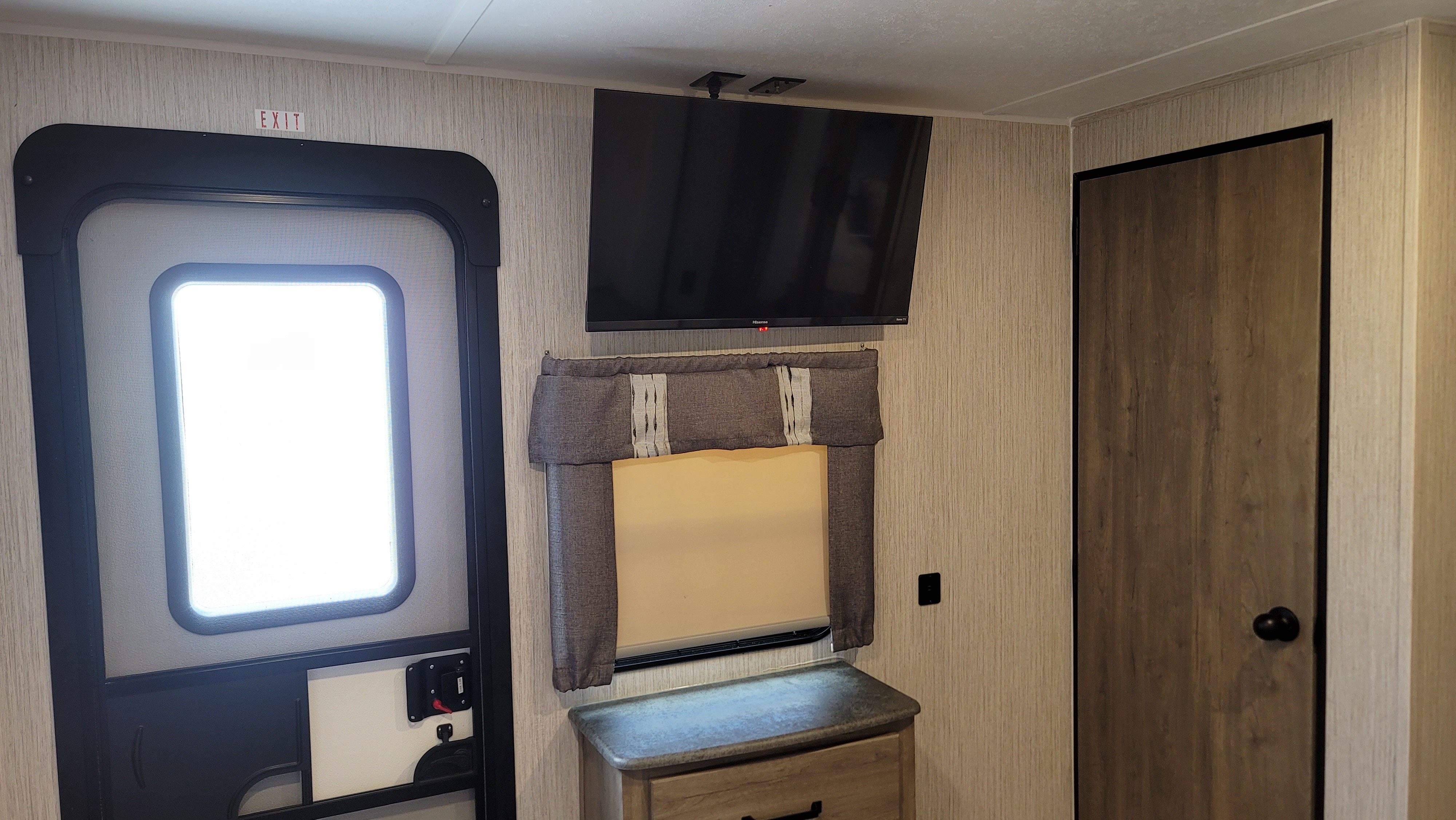 RV rental interior: an exit door with 'EXIT' sign, TV, window, and a wood-paneled interior door.. Forest River Palomino Puma 2022