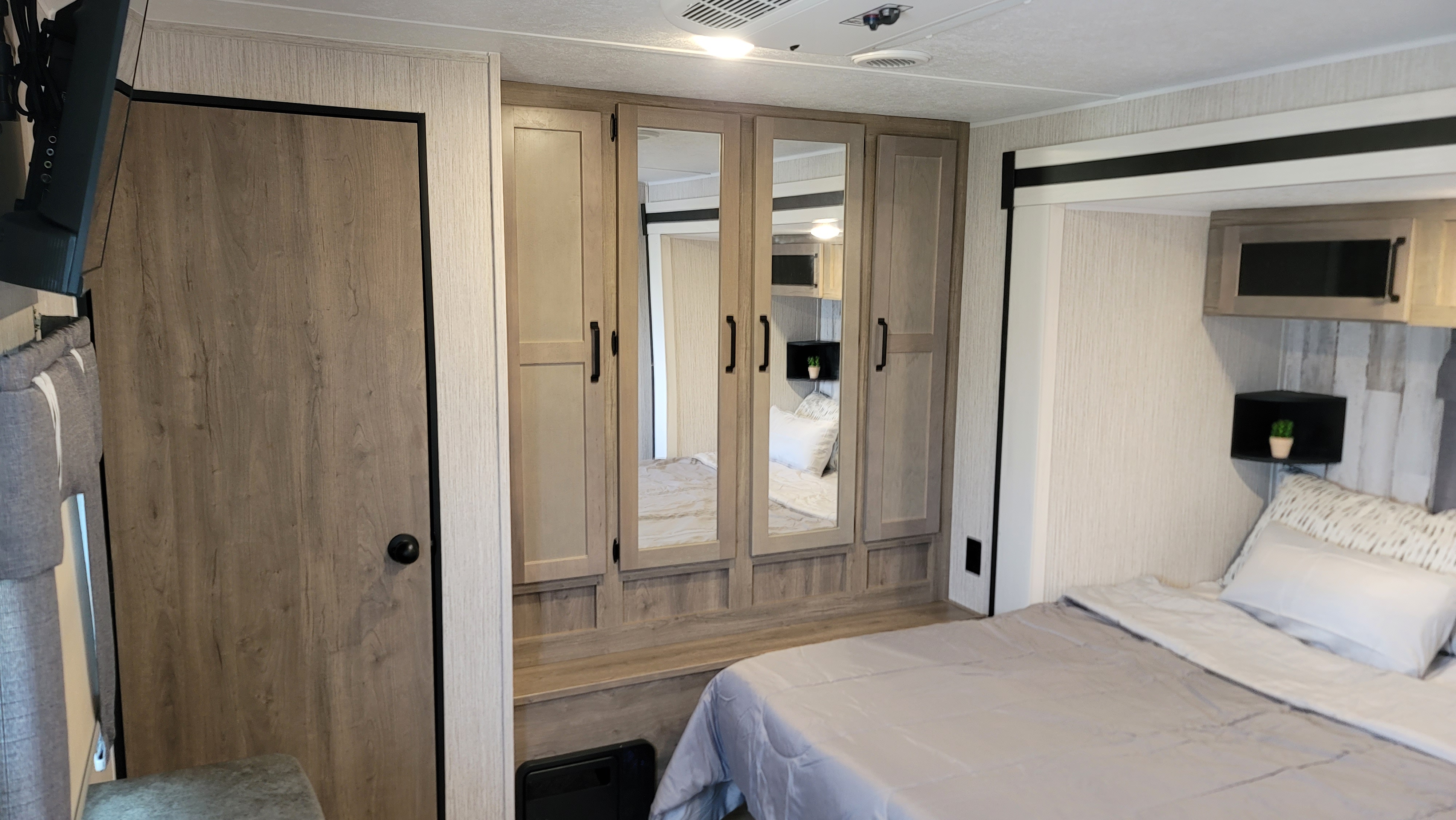 RV rental bedroom interior: light wood wardrobe with mirrors, comfy bed, overhead cabinets, and TV create a functional, cozy space.. Forest River Palomino Puma 2022