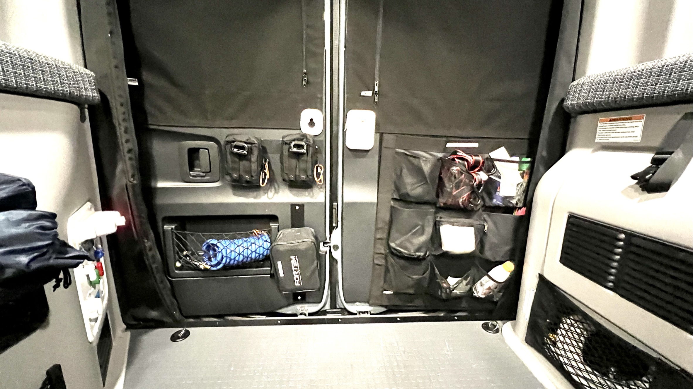 RV rental interior: organized rear doors with blackout shades. Various storage includes tactical pouches, nets, and multi-pocket organizers.. Winnebago Revel 2022