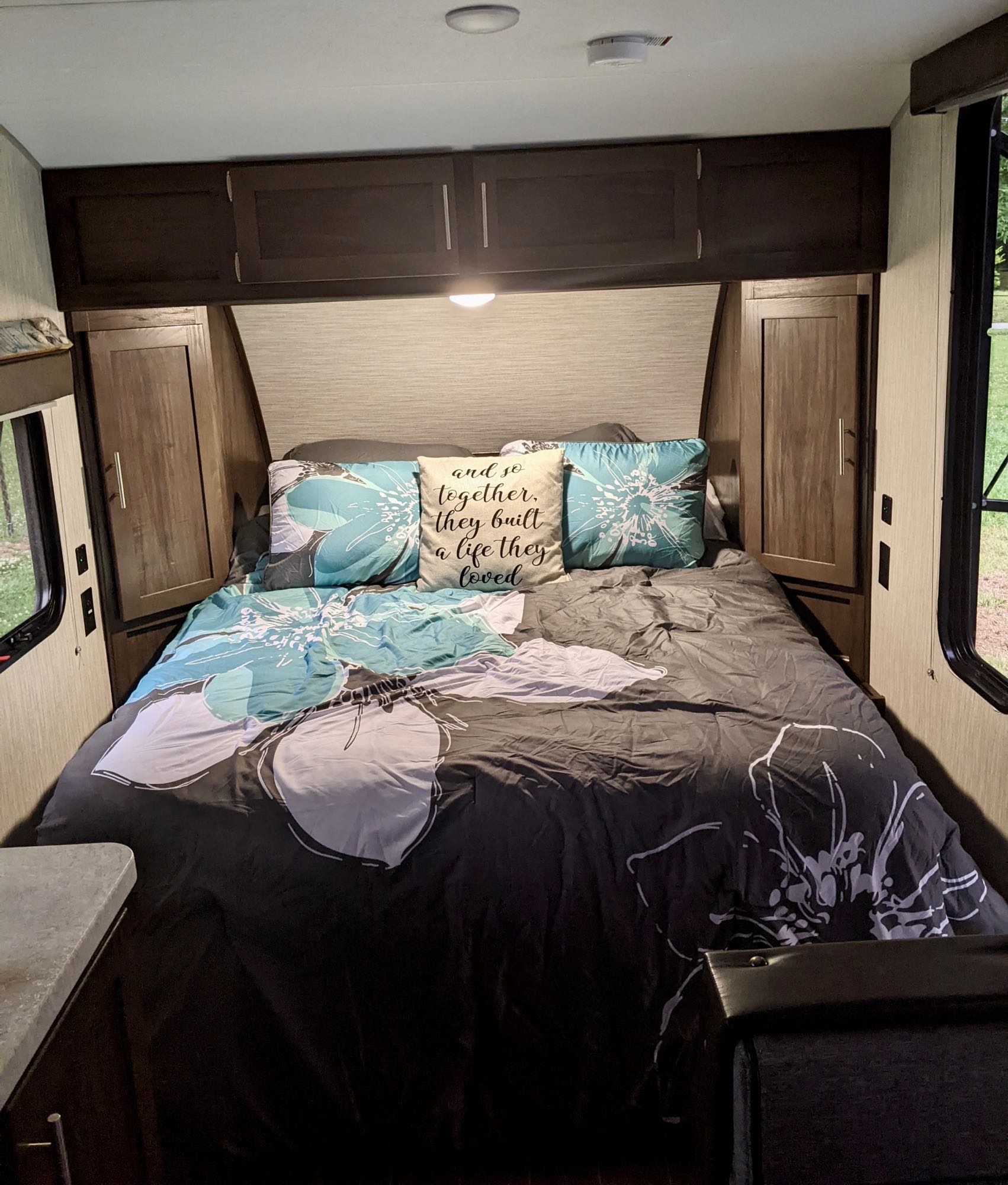 Cozy RV rental bedroom, featuring a comfy bed with floral bedding, overhead storage, and side windows.. Forest River Cherokee Wolf Pup 2019