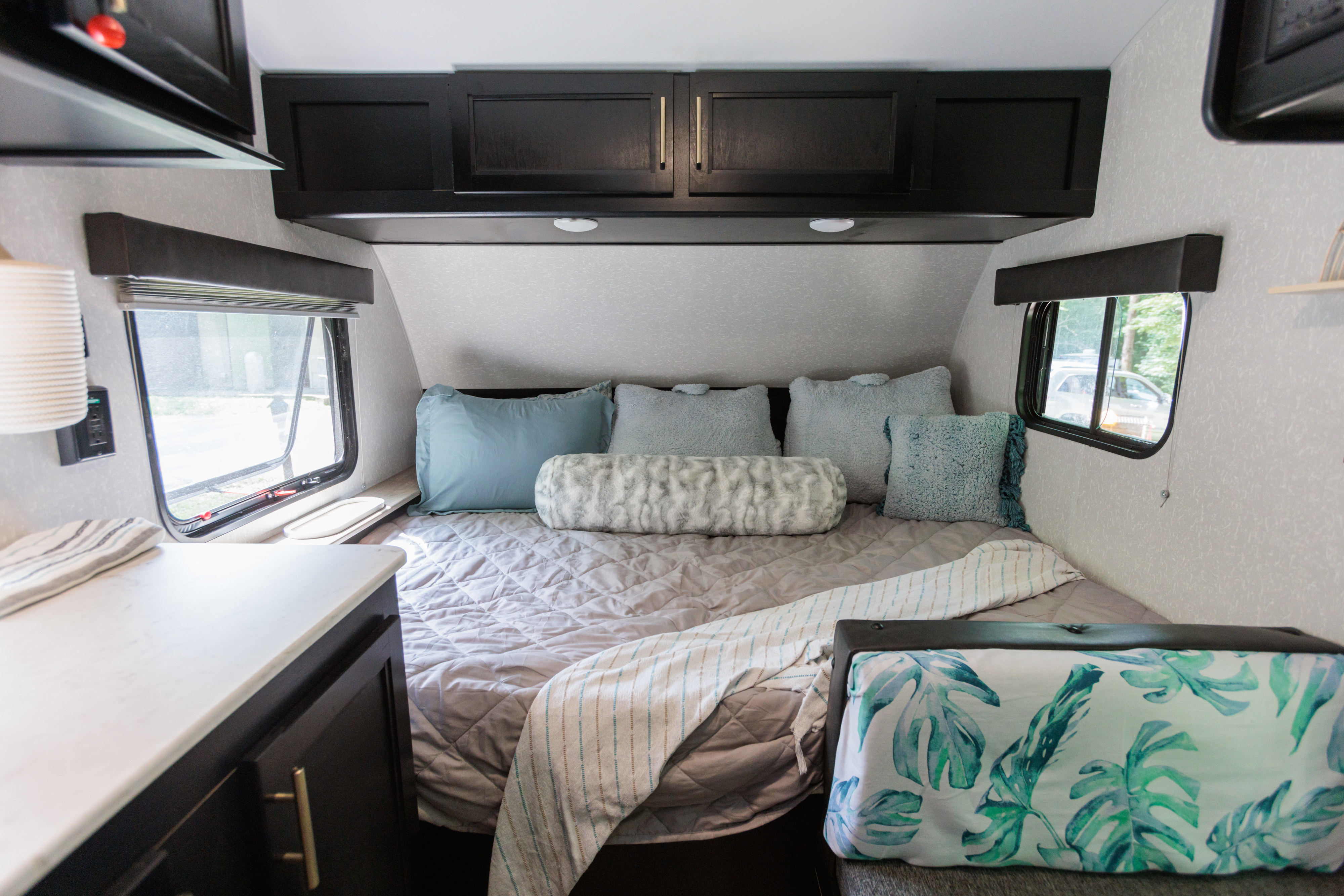 Cozy and modern RV rental bedroom featuring a queen bed, blue and grey pillows, and sleek dark cabinets. Ideal for comfortable travel.. Forest River Cherokee Wolf Pup 2022