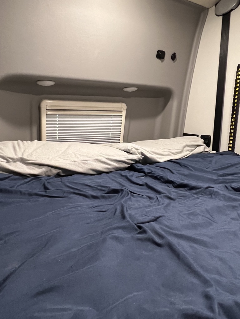 Cozy RV rental bedroom interior with a comfortable bed, pillows, and a window with blinds.. Winnebago Revel 2022