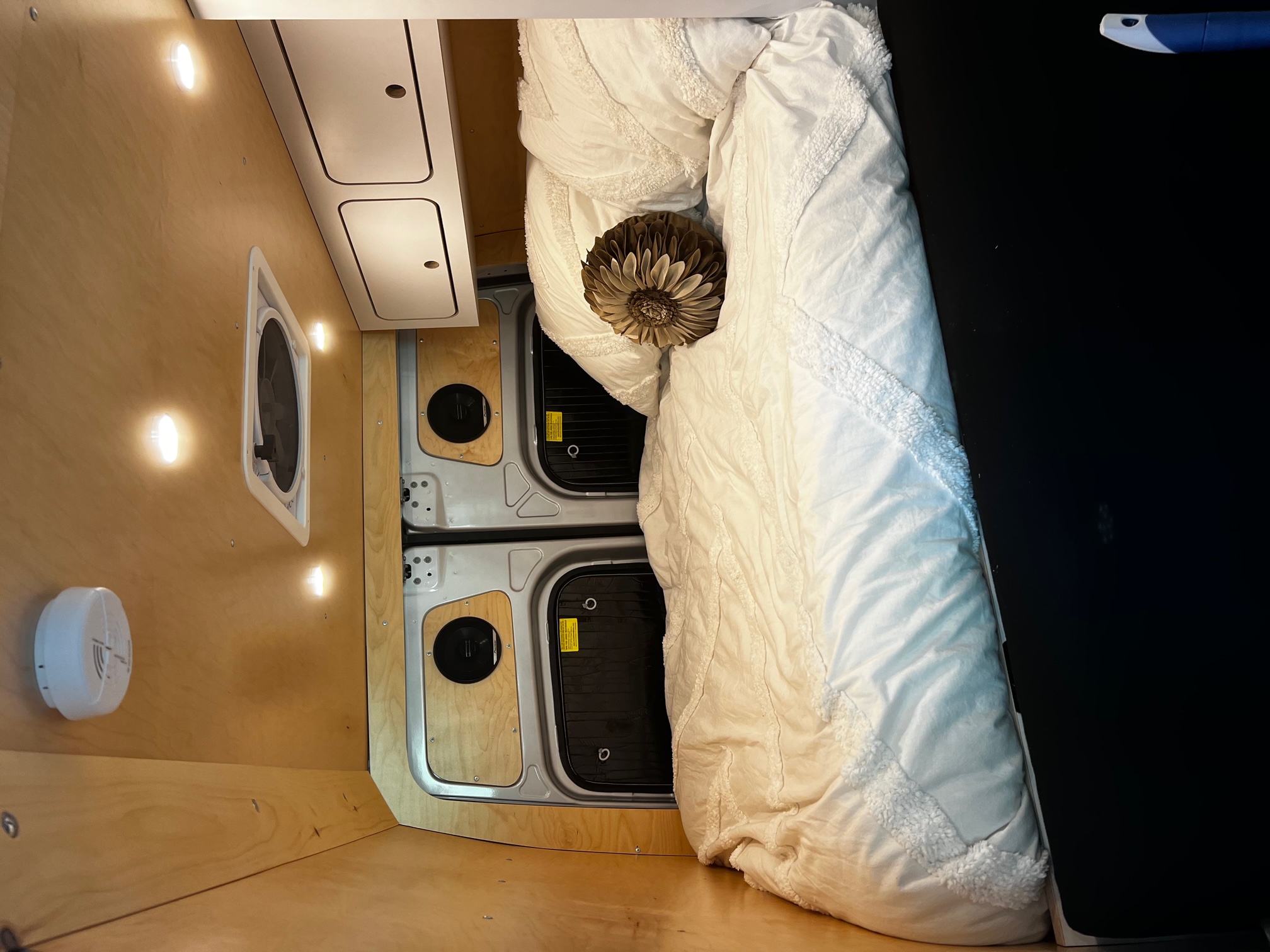 Inside a cozy RV rental: light wood walls, bright lights, ceiling fan, and a comfy bed with a decorative pillow. Perfect camper van setup.. VanCraft Mercedes Benz 2022