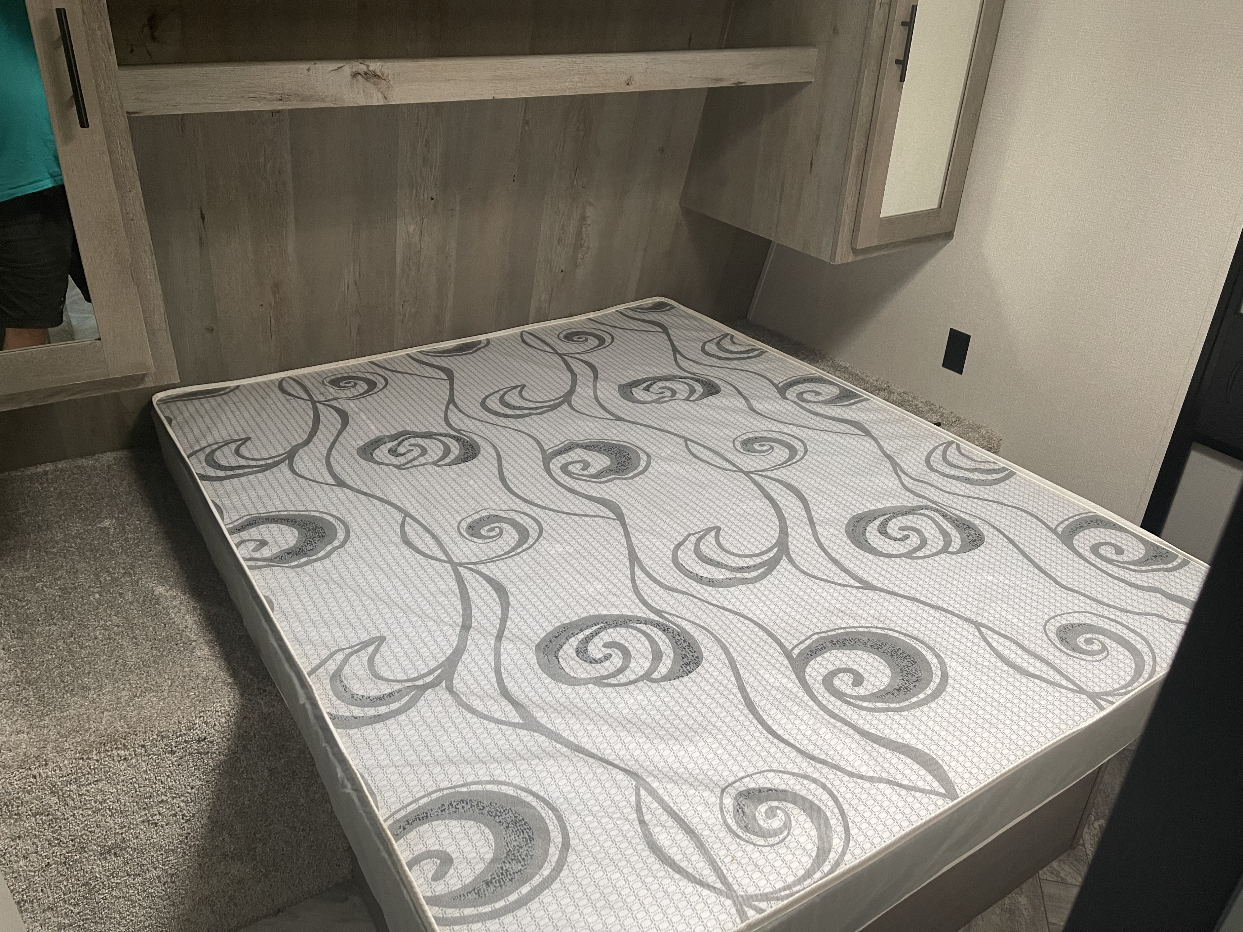 RV rental bedroom featuring a patterned mattress, overhead cabinetry, and mirror for compact living.. Keystone 280BH Springdale 2021