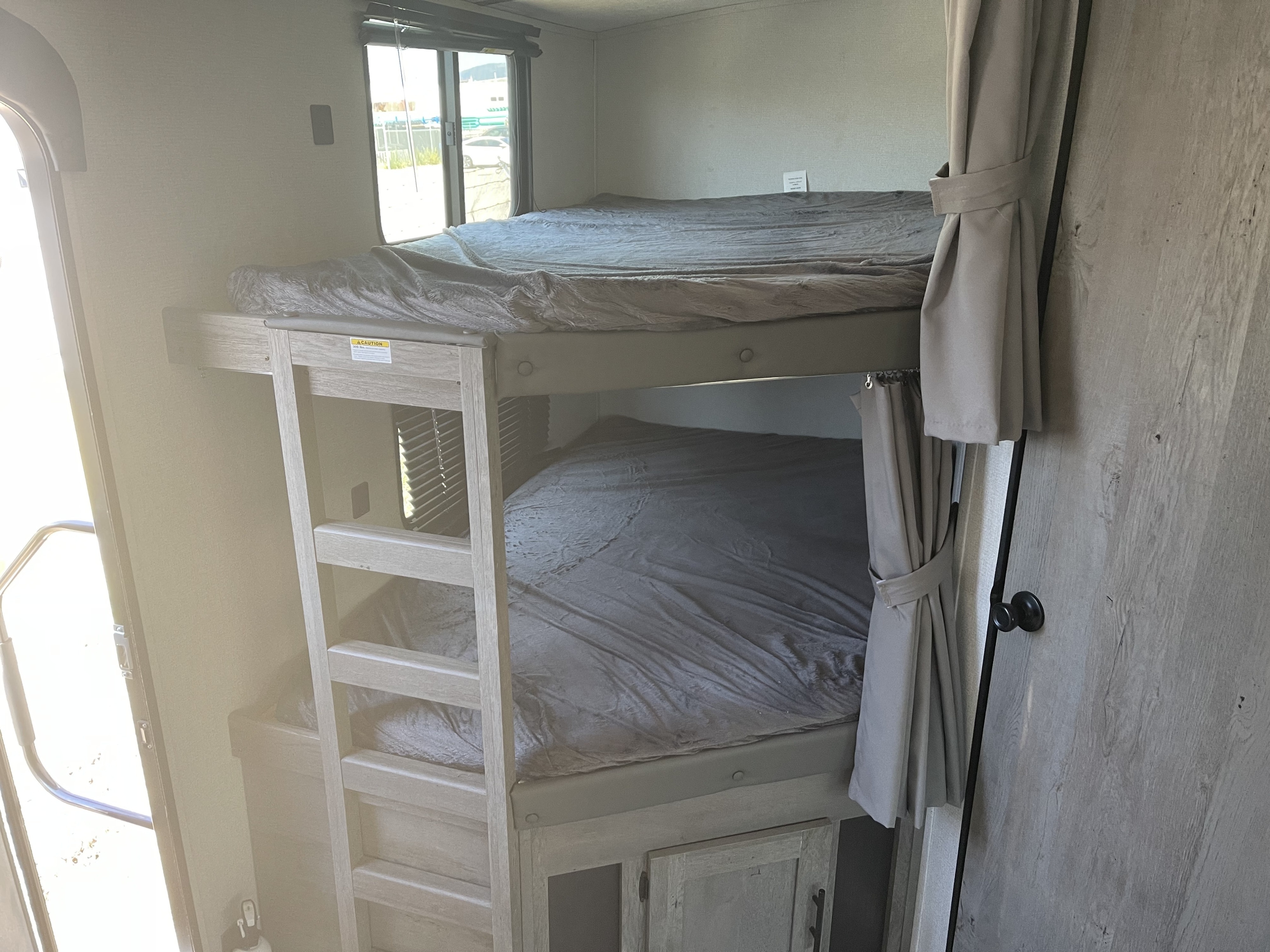 Cozy rv rental interior featuring comfortable bunk beds with gray bedding and a ladder, perfect for families.. Keystone 280BH Springdale 2021