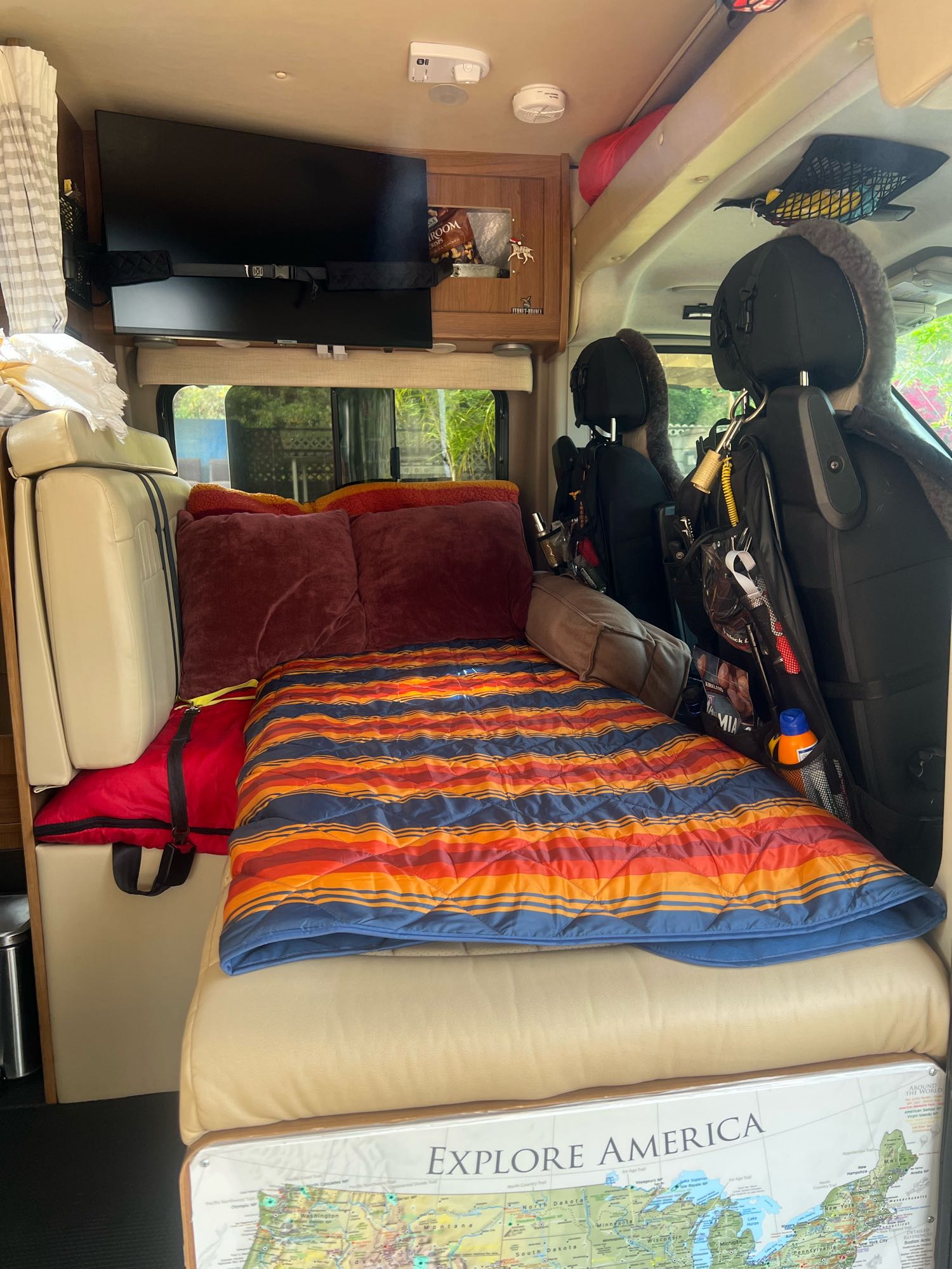 Compact RV rental interior featuring a bed with striped comforter, mounted TV, and clever storage solutions for travel.. Winnebago Travato 2014