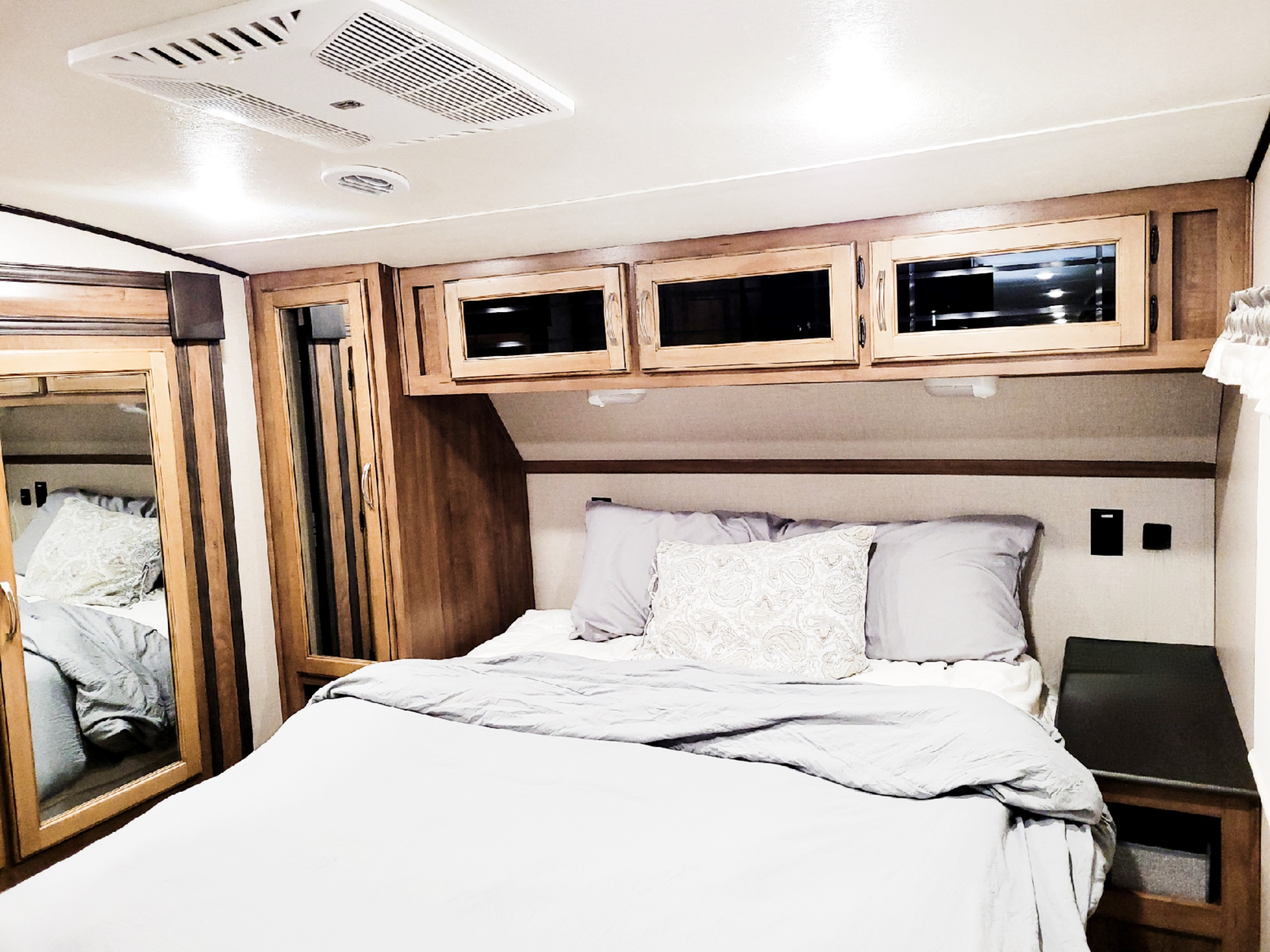 Cozy RV rental bedroom featuring a neatly made bed, overhead cabinets, and a mirrored wardrobe.. Coachmen Chaparral 2020