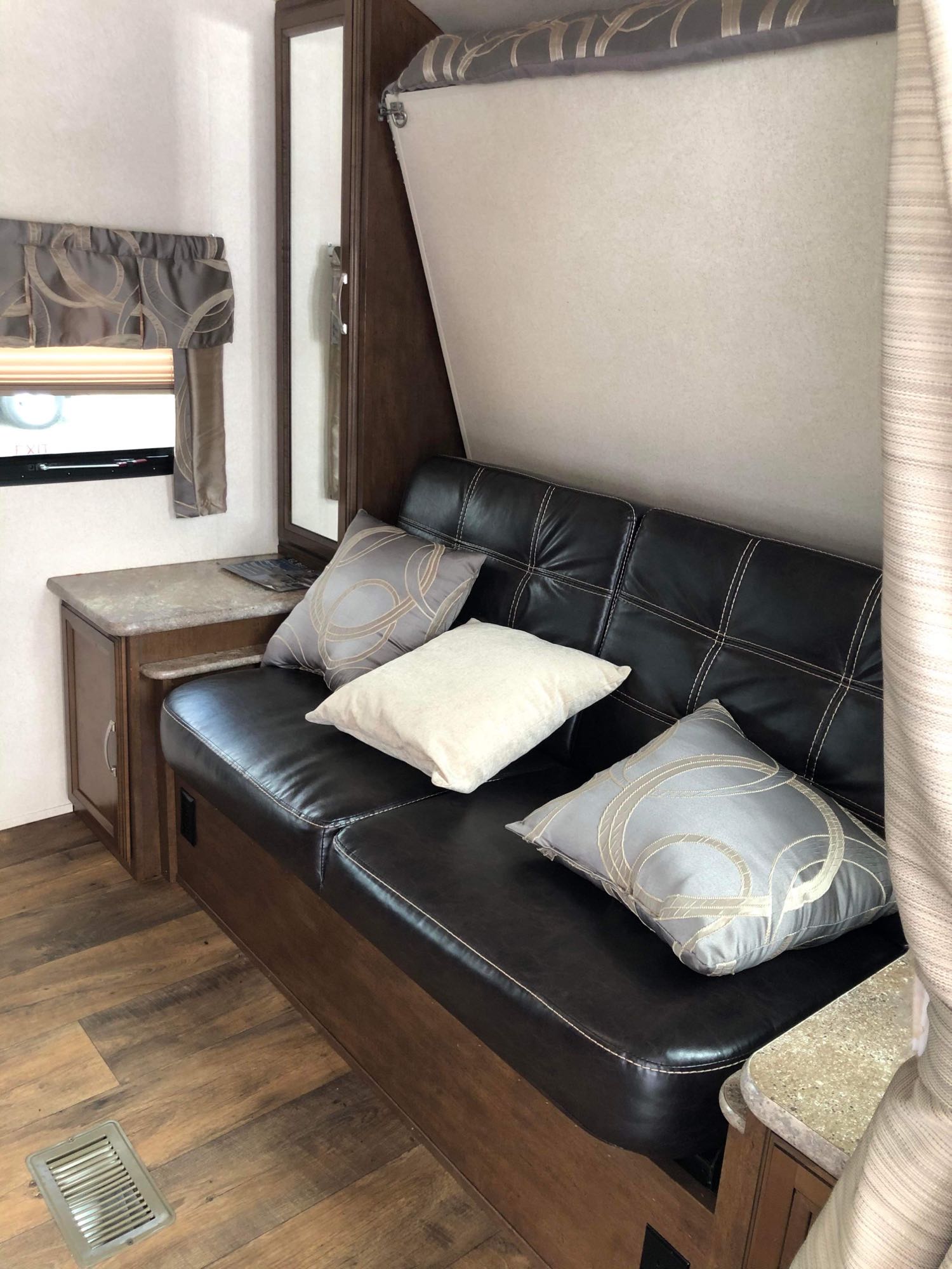 Compact RV rental interior: dark sofa, patterned pillows, wood cabinets, and laminate flooring.. Forest River Salem Hemisphere Hyper-Lyte 2019