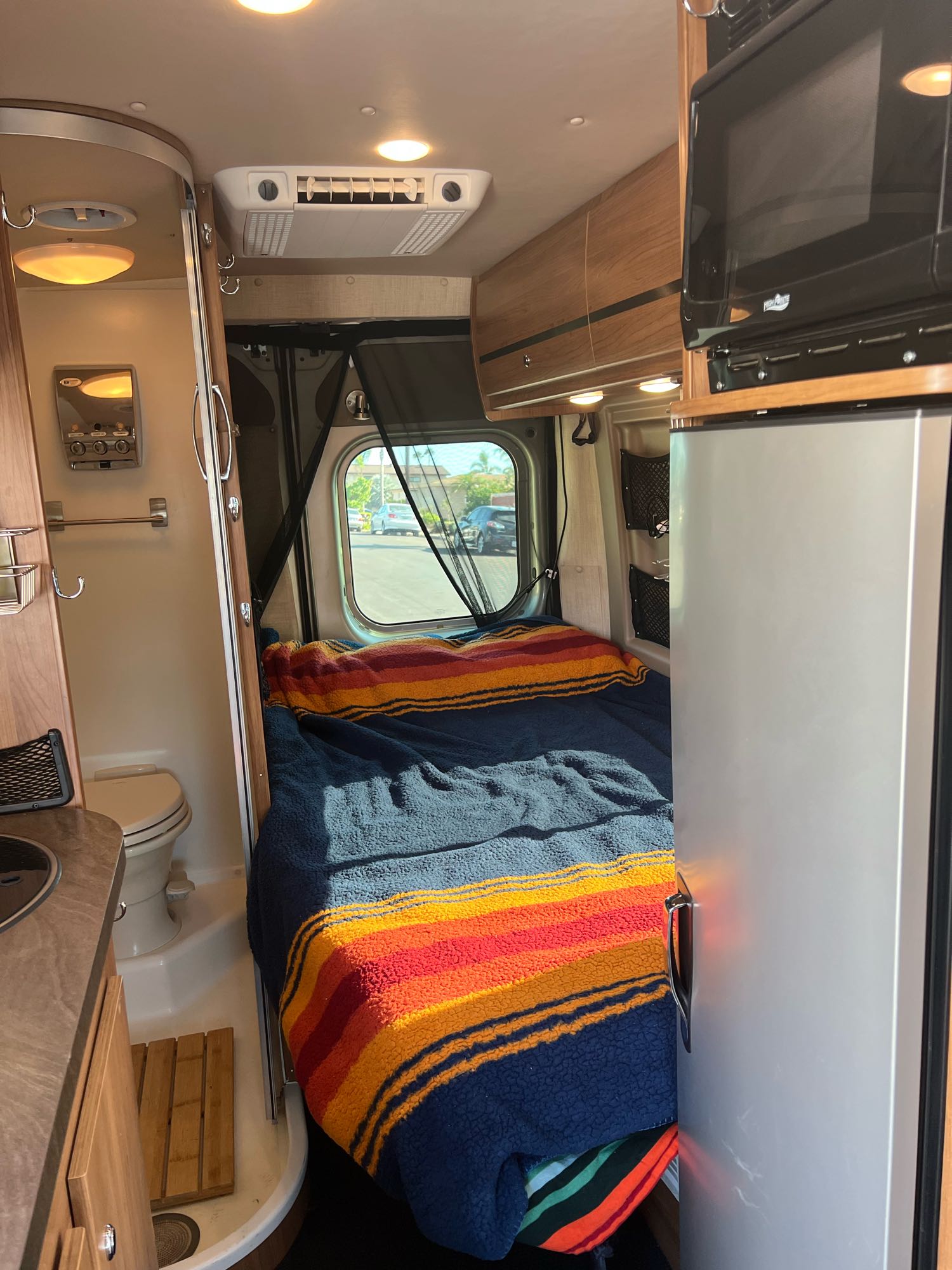 Cozy RV rental interior: bed, wet bath, microwave, fridge, and overhead storage. Perfect for road trips and compact living.. Winnebago Travato 2014